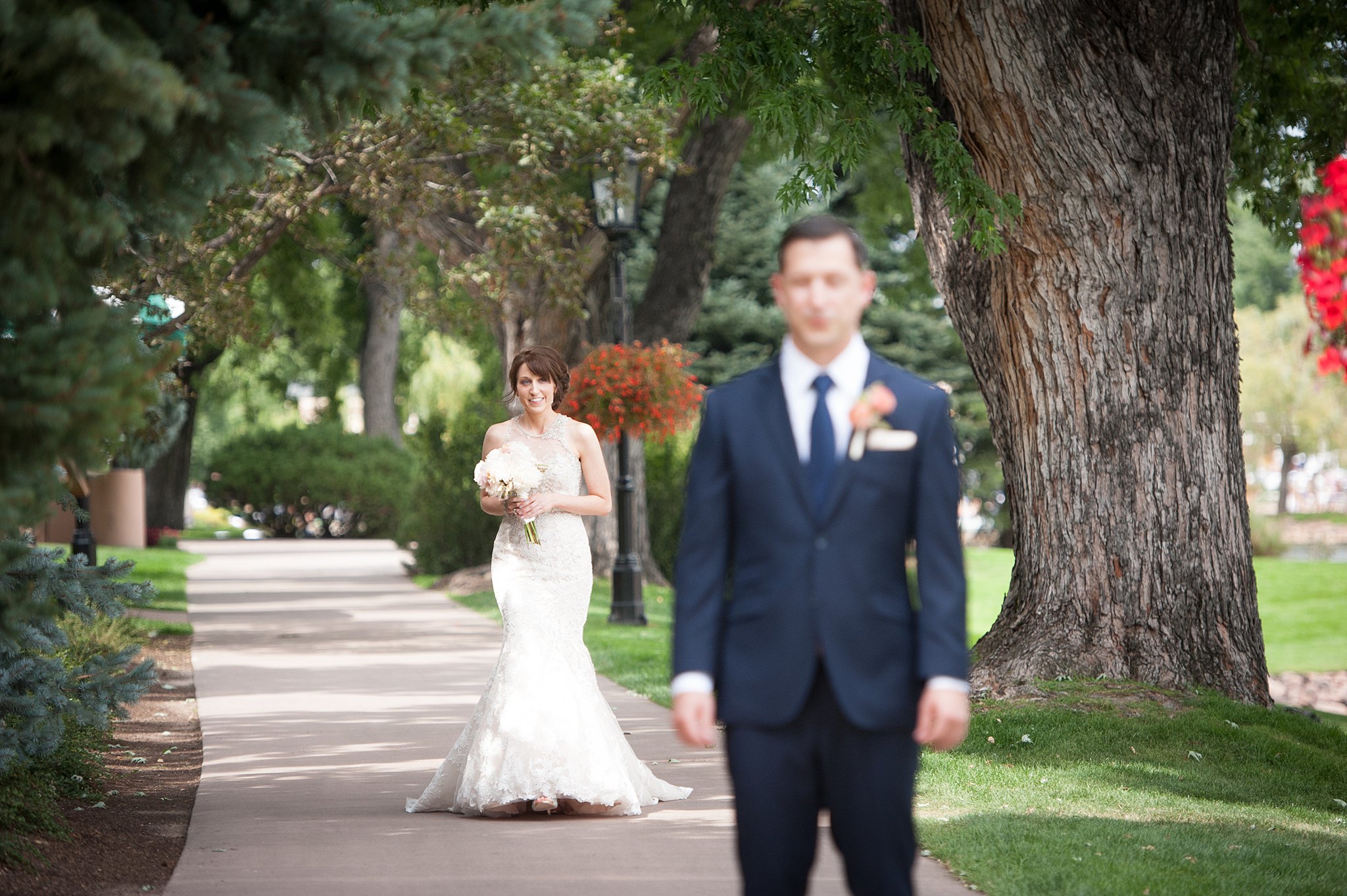 A groom smiles while walking towards her groom as he waits for their first look on a sidewalk