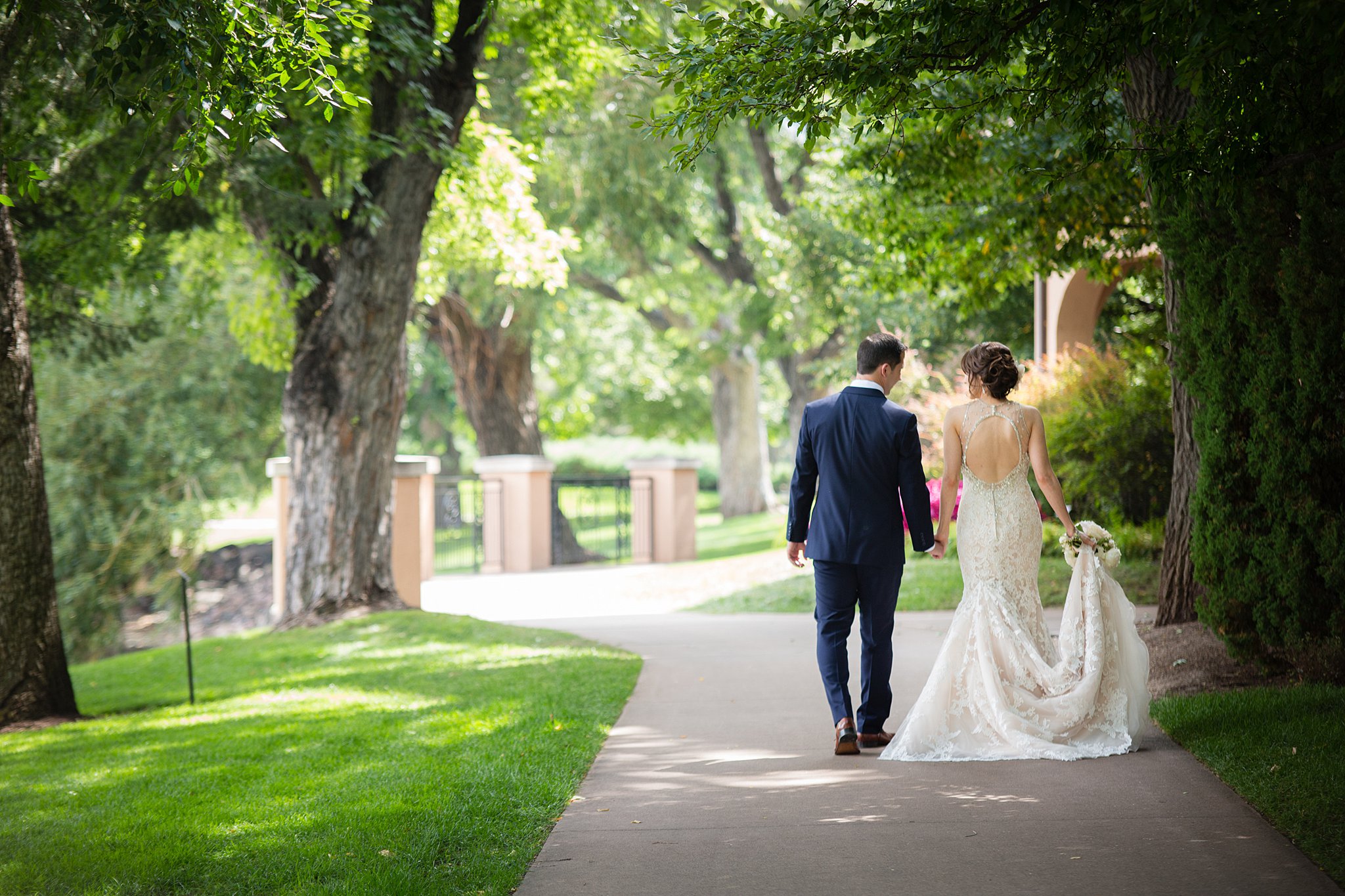 Newlyweds hold hands and the dress train as they chat walking down the sidewalk at their The Broadmoor Wedding