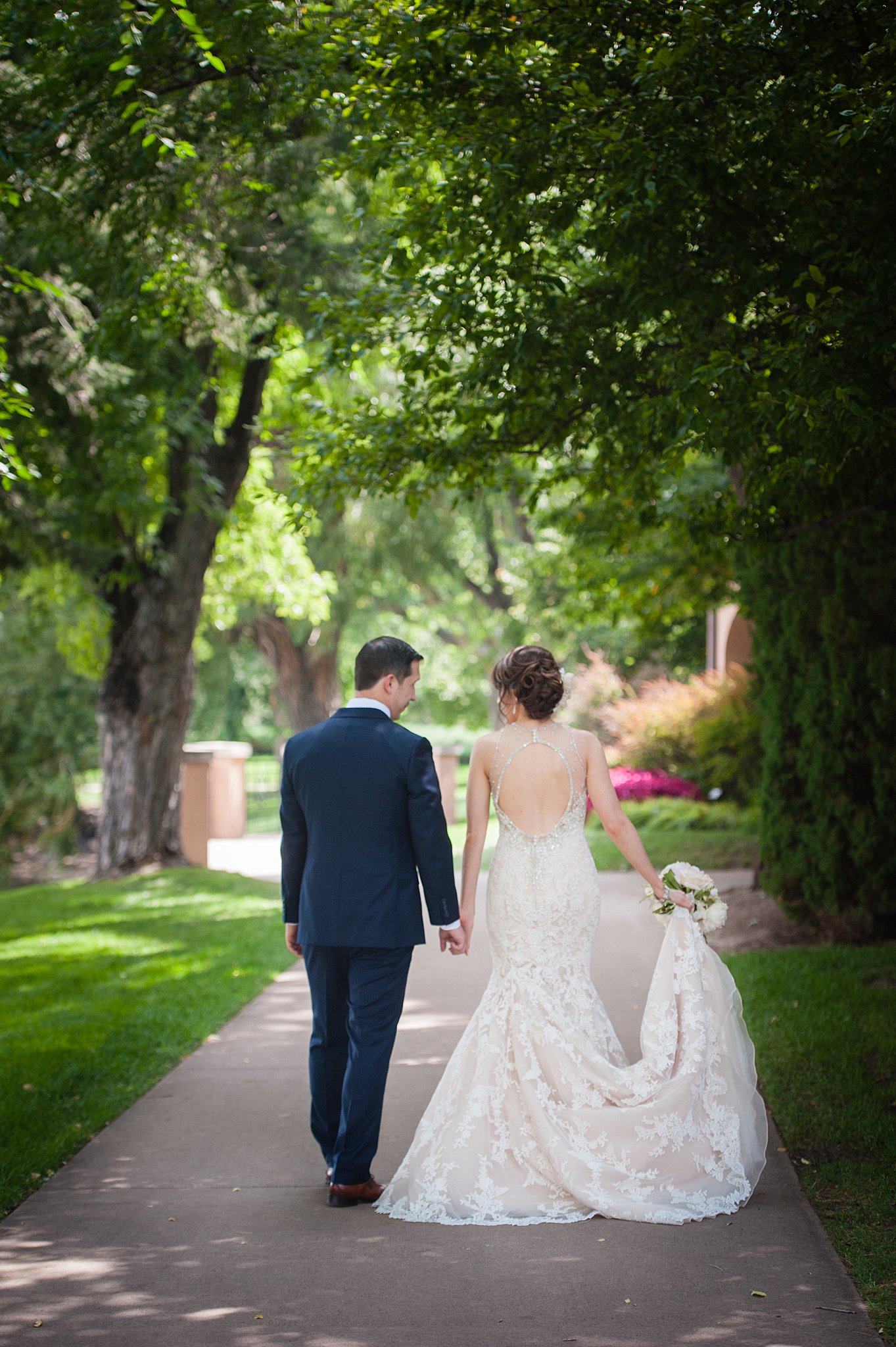 Newlyweds hold hands and the dress train as they chat walking down the sidewalk