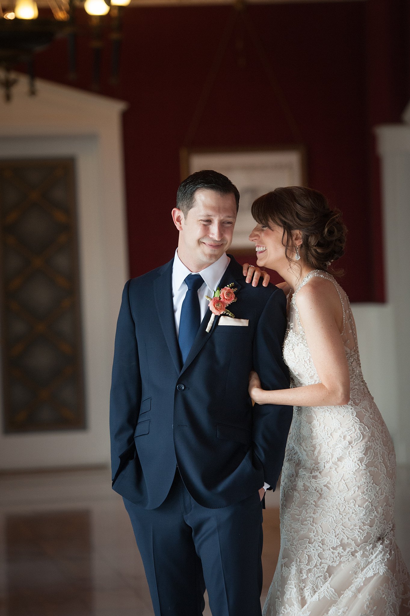 A bride laughs on the shoulder of her groom as they stand in a lobby