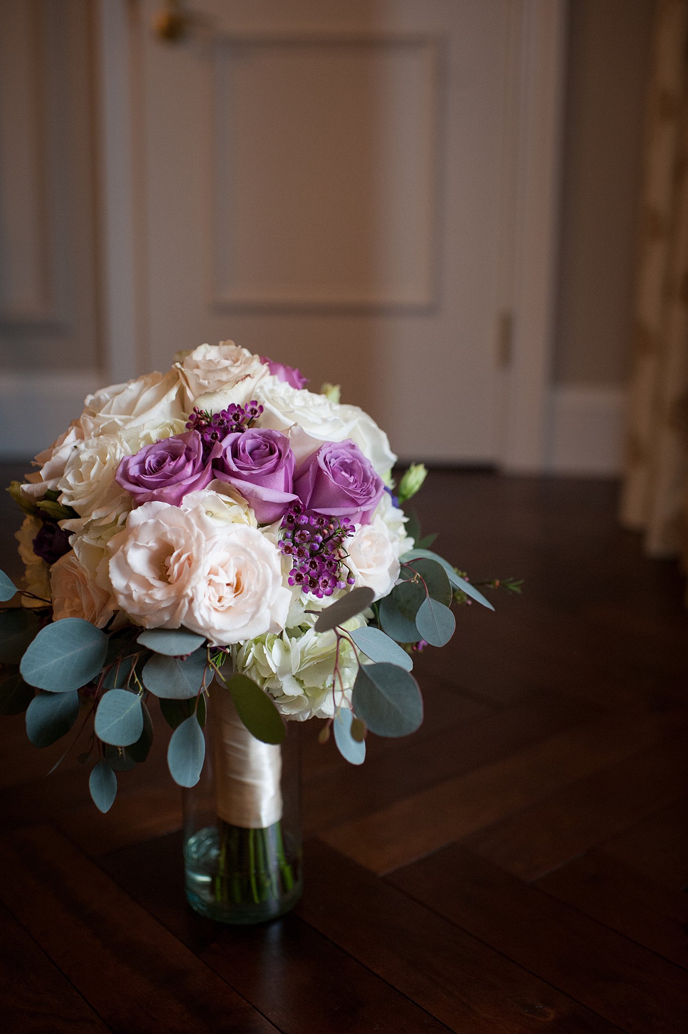 Details of a bride's purple, pink and white bouquet standing in a vase on a table