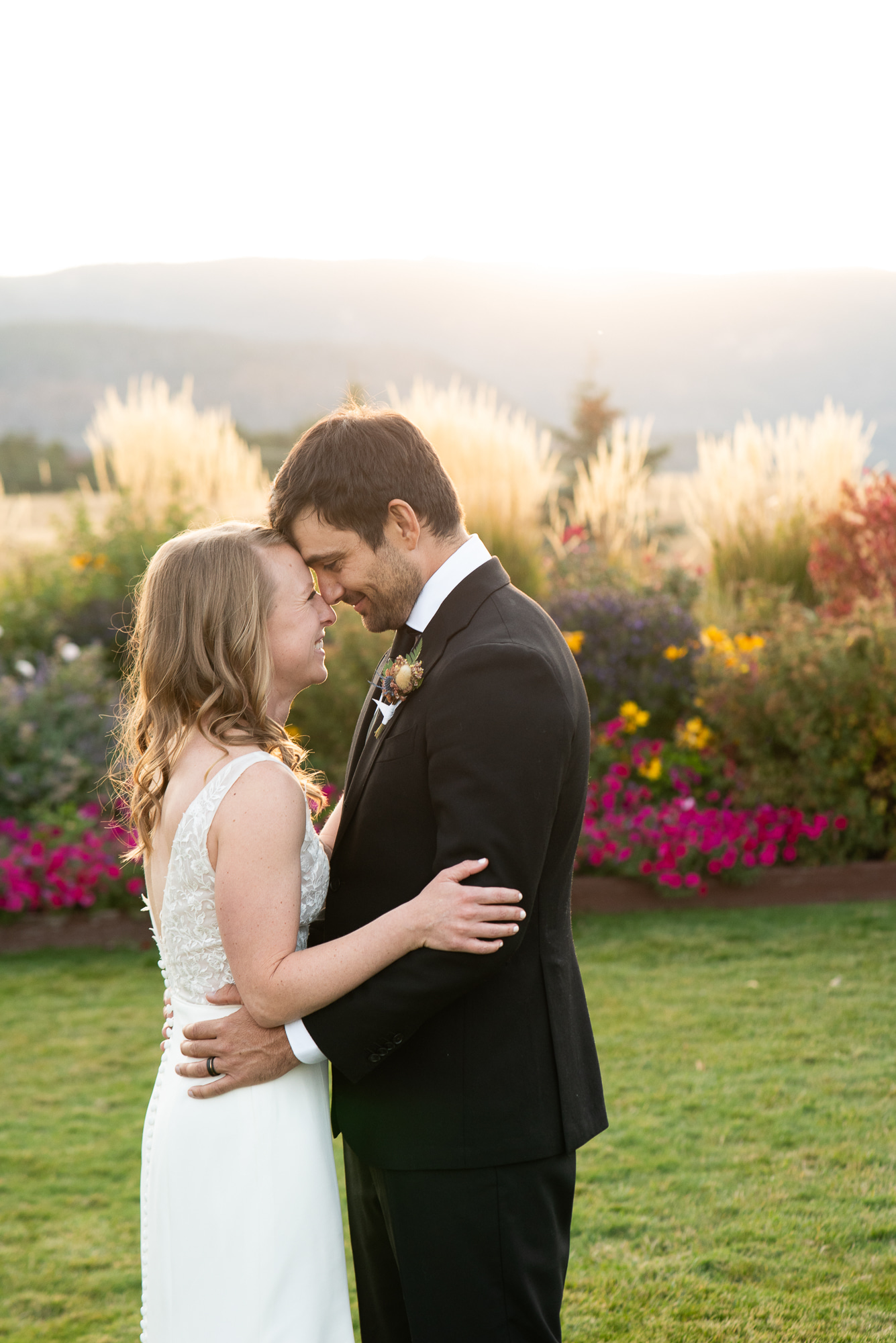 Newlyweds touch foreheads while giggling in a garden of flowers at The Venue At Crooked Willow Farms Wedding