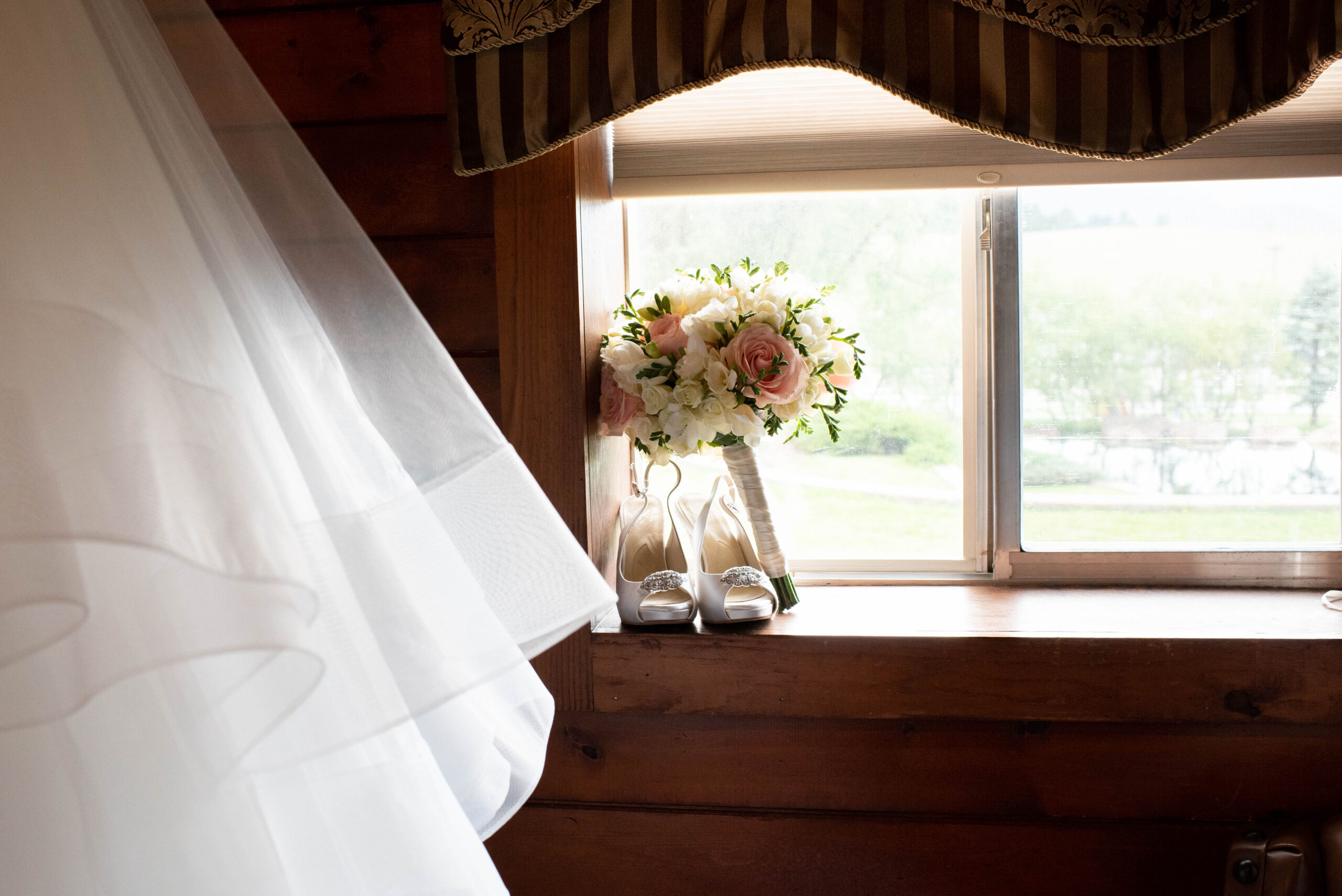 Details of a bride's shoes and pink bouquet sitting in a window sill