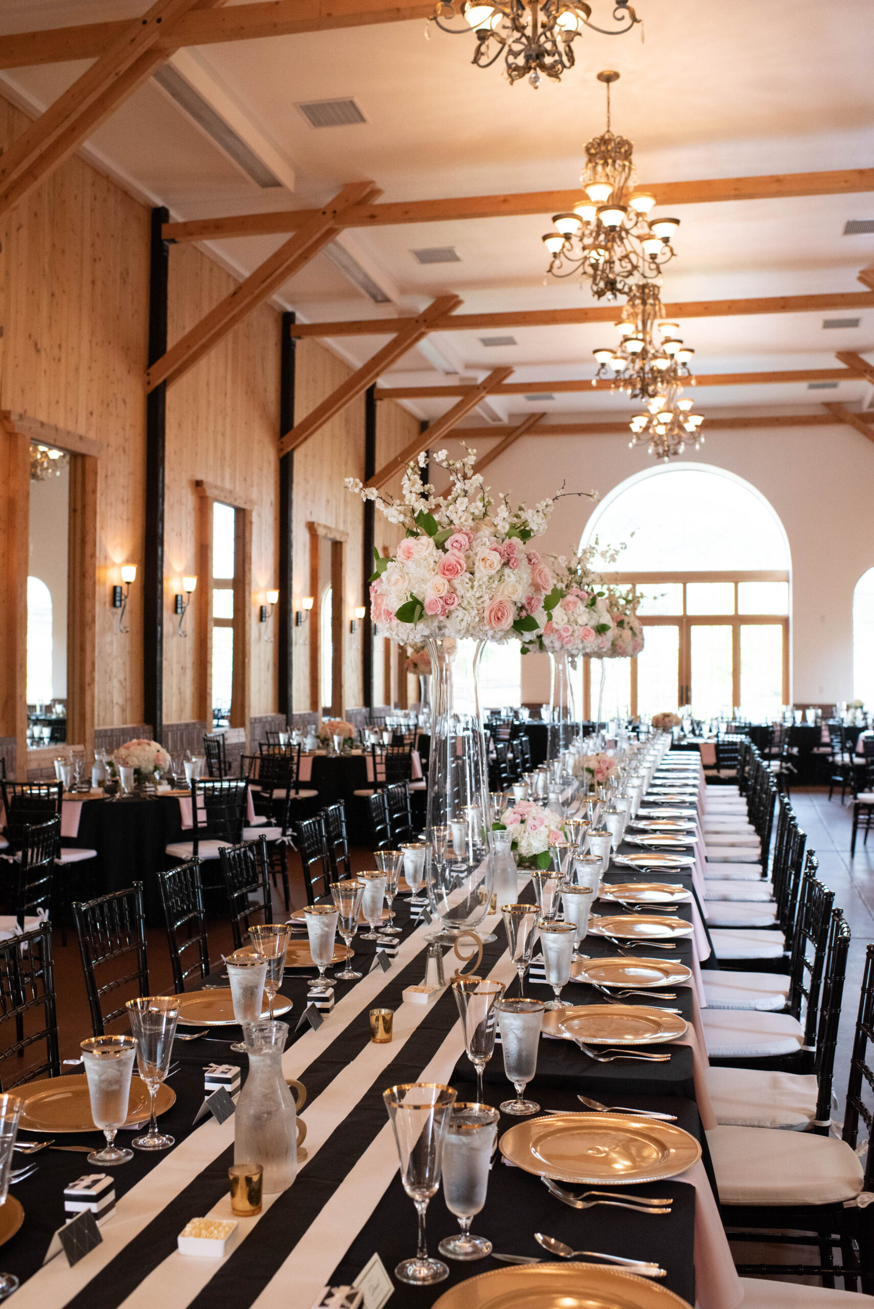 Details of a long reception table in the center of the room at The Venue At Crooked Willow Farms Wedding with black linen and pink napkins