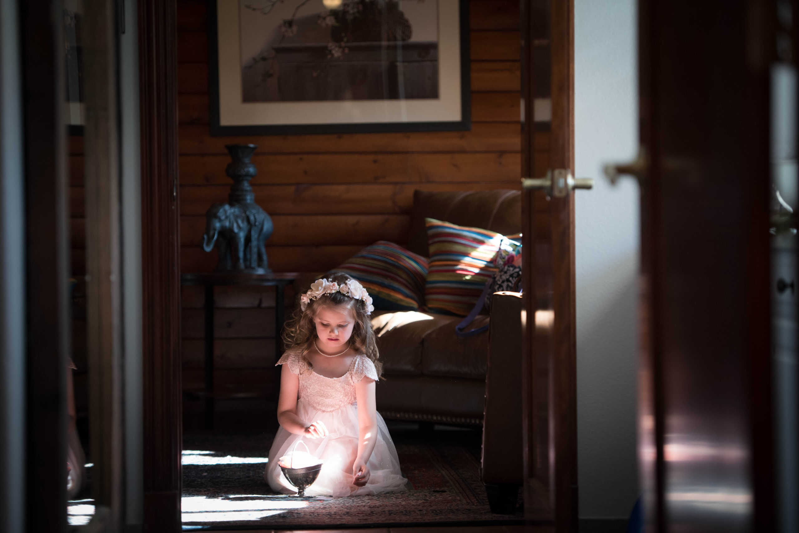 A young girl prepares her flower bucket on the floor in a pink dress