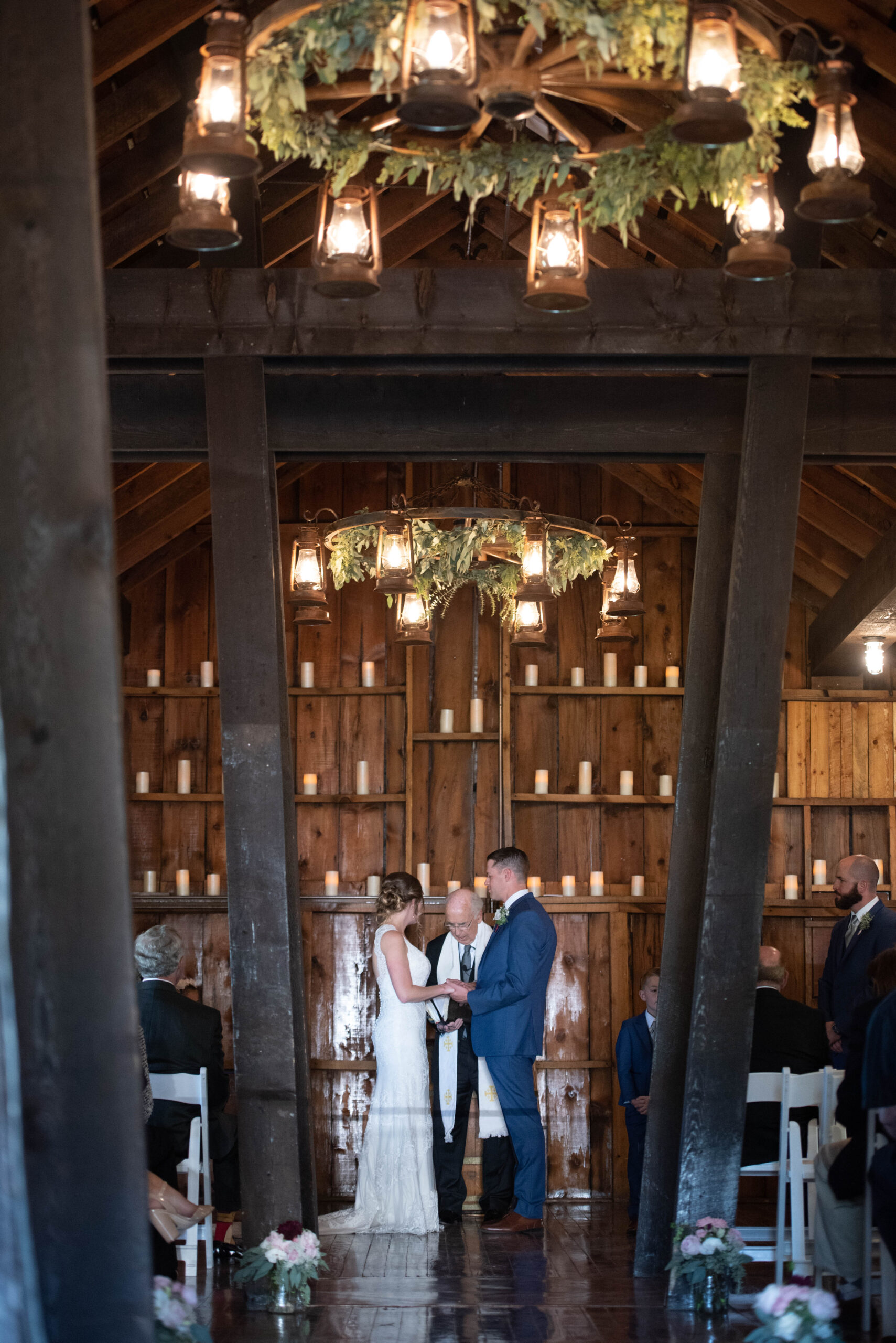 A bride and groom in a blue suit hold hadns at the altar under chandeliers at The Venue At Crooked Willow Farms Wedding