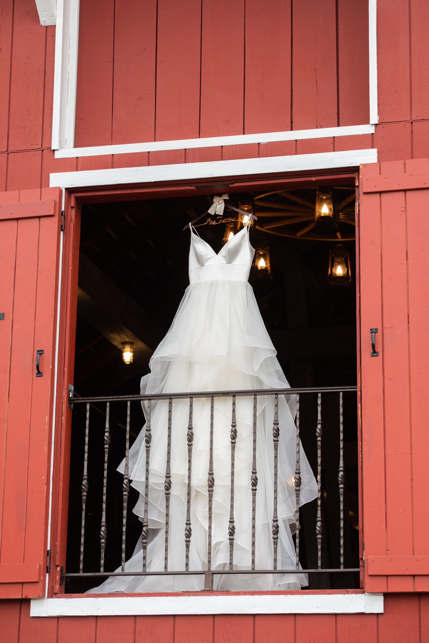 A wedding dress hangs in a barn window at The Venue At Crooked Willow Farms Wedding