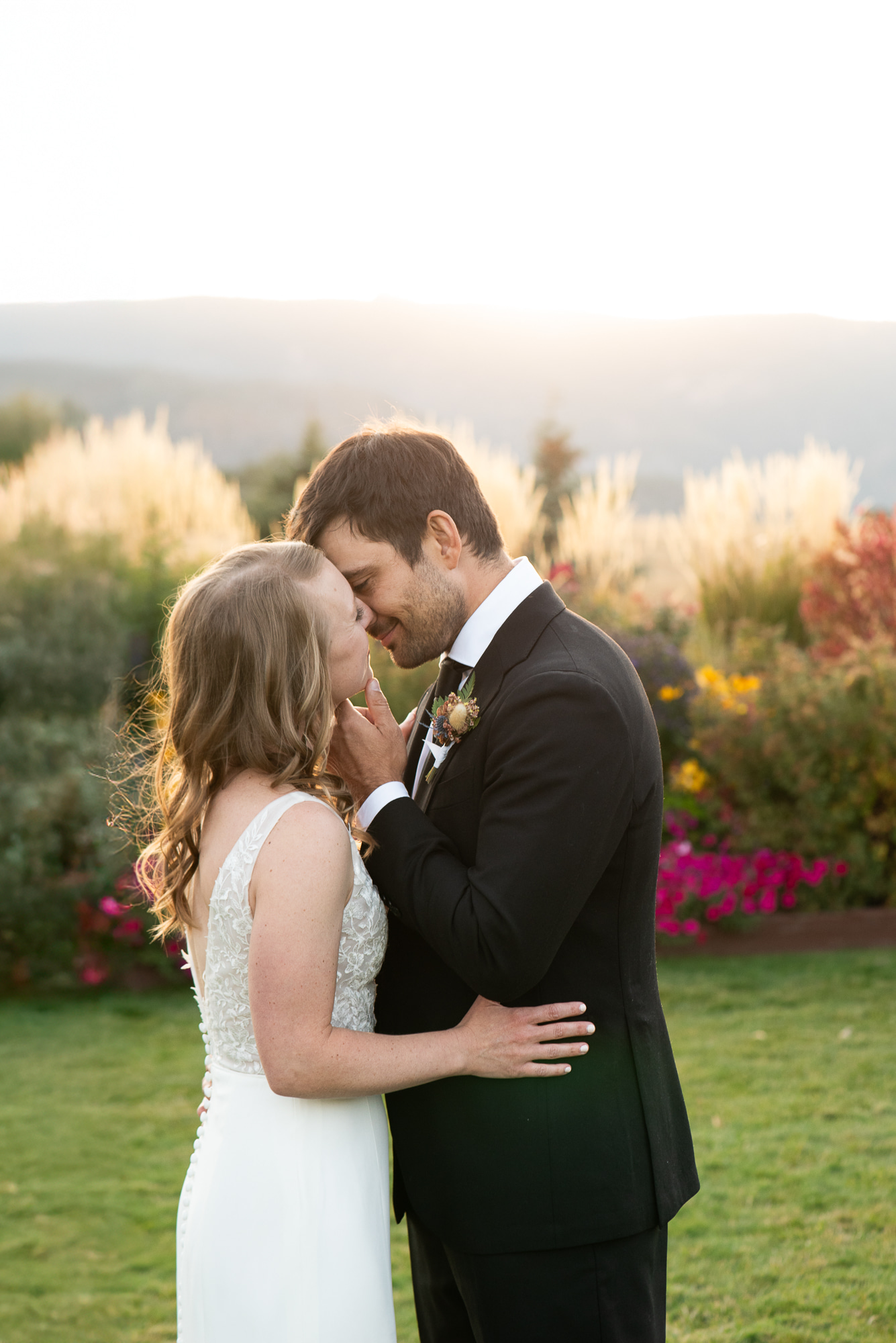 A bride and groom lean in for a happy kiss in a garden at sunset