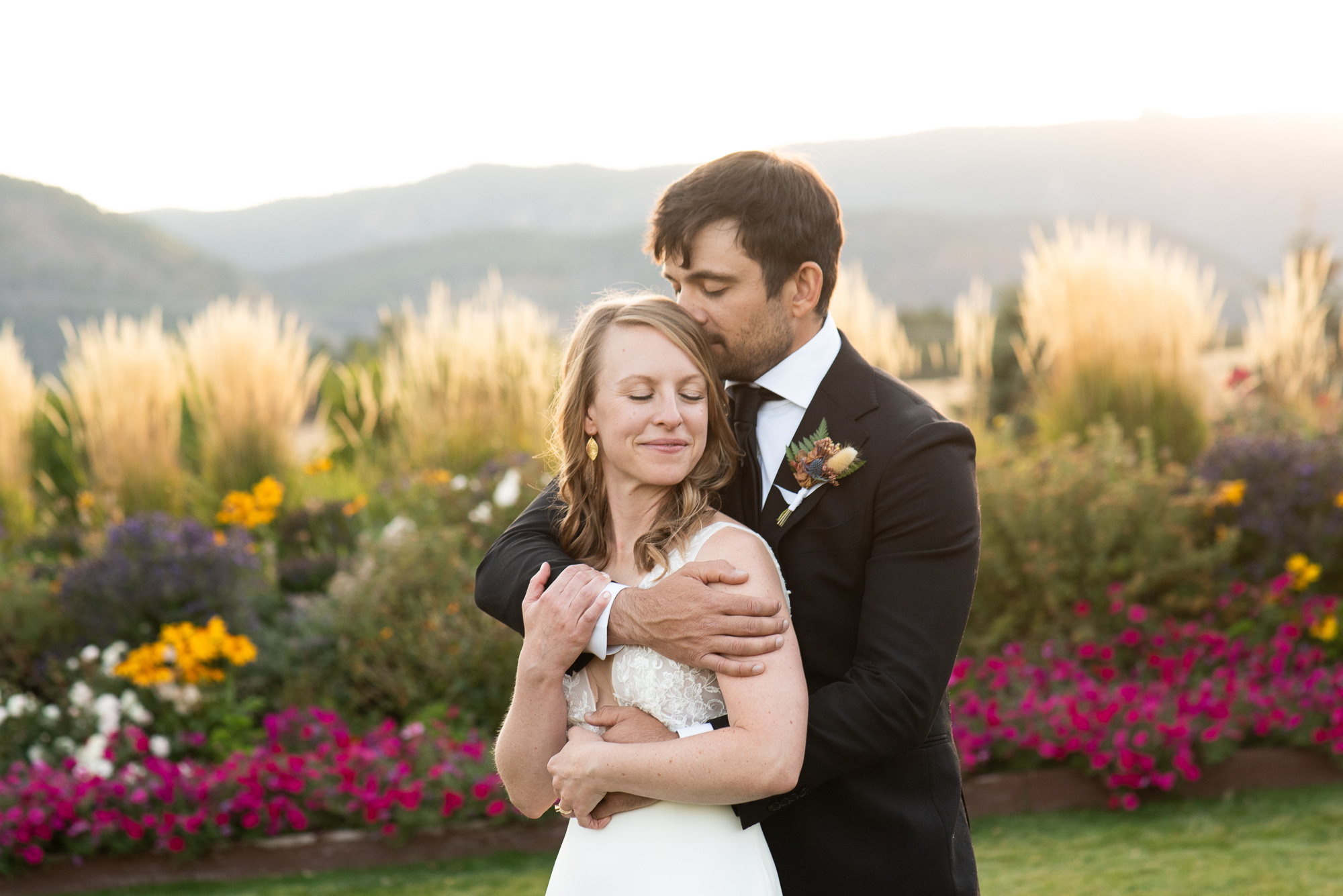 Newlyweds snuggle in a vibrant garden in the mountains at sunset at their The Venue At Crooked Willow Farms Wedding