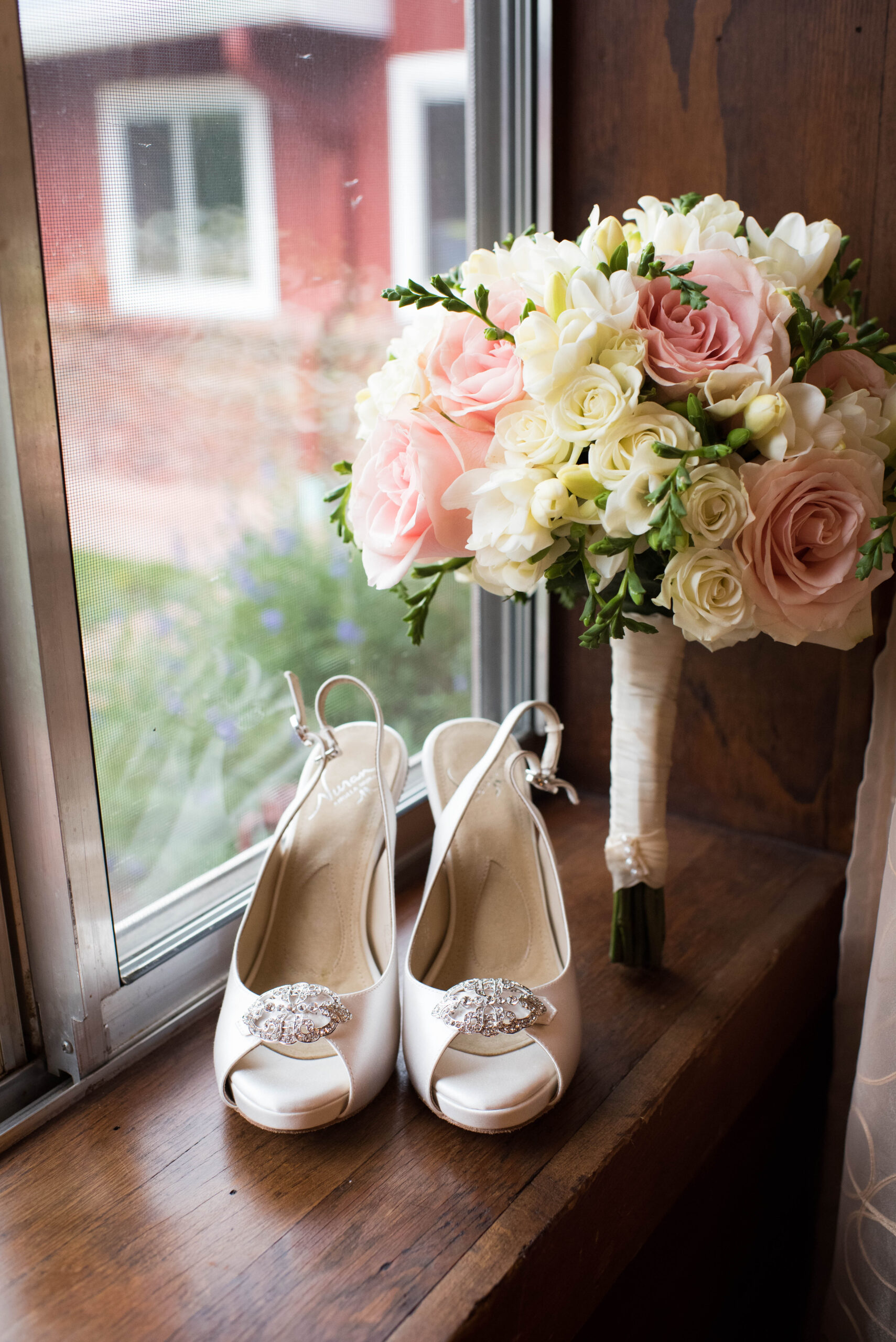 Details of a bride's white shoes and pink and white bouwuet sitting in a window sill