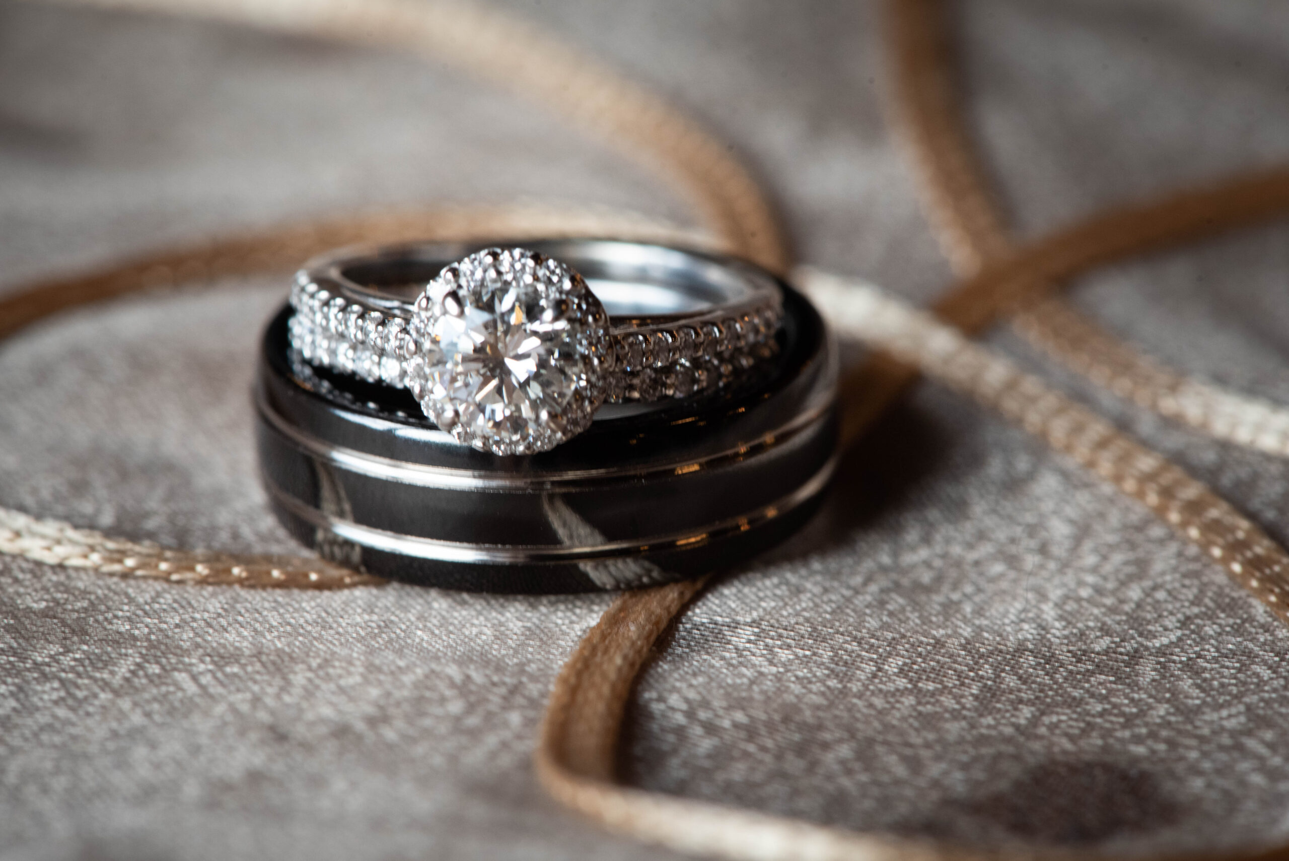 Details of a bride's engagement ring sitting on a groom's black wedding band