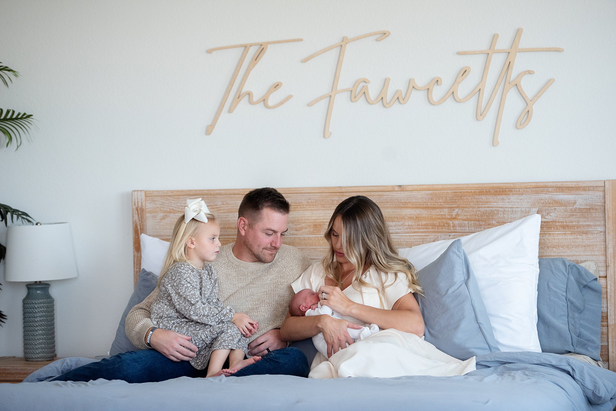 A happy family sits on a bed with the toddler in dad's lap and newborn in mom's arms after visiting denver baby boutiques