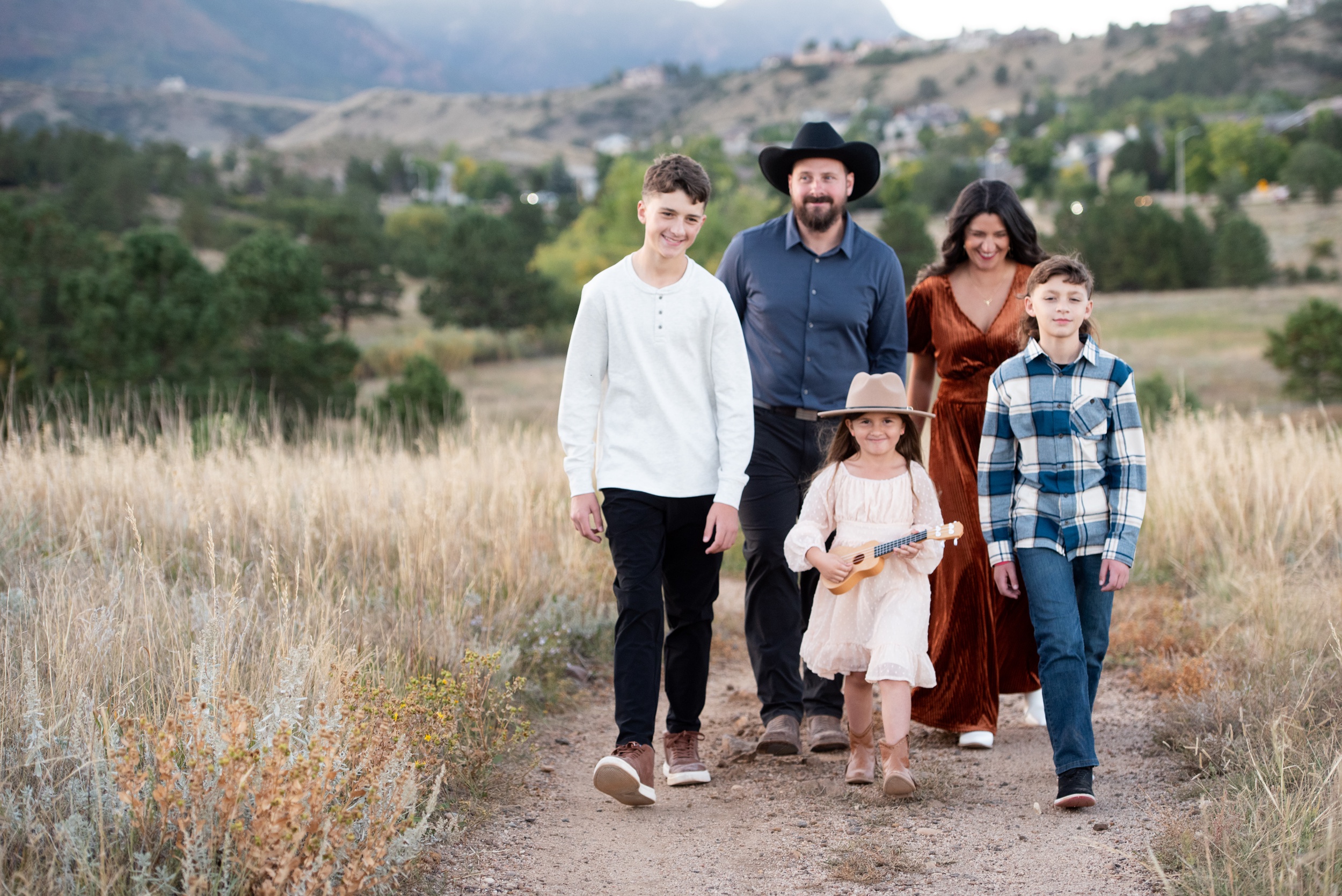 A happy family of 5 laughs while walking in a mountain park trail