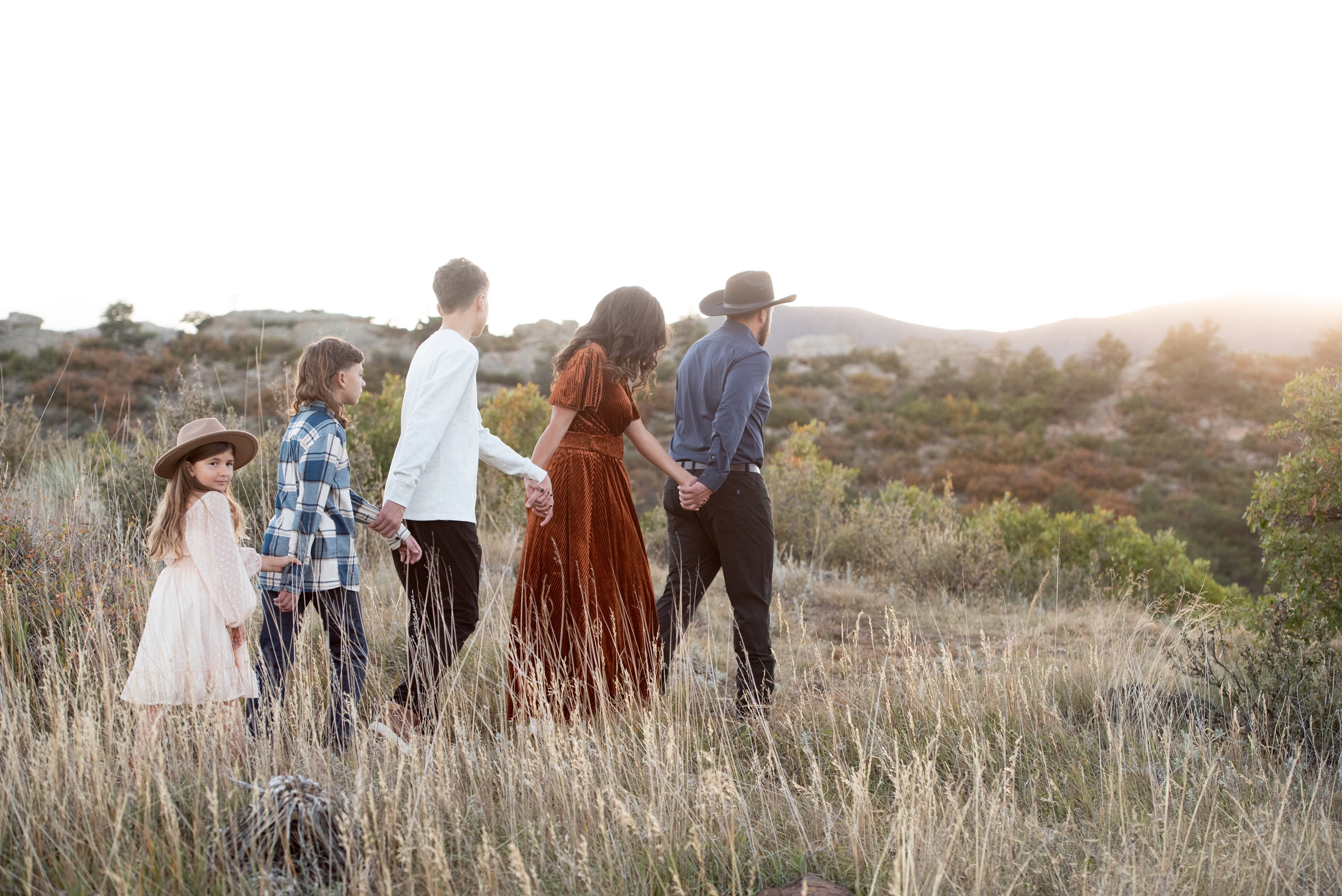 A father leads his family of 5 through tall golden grass at sunset after visiting denver toy stores