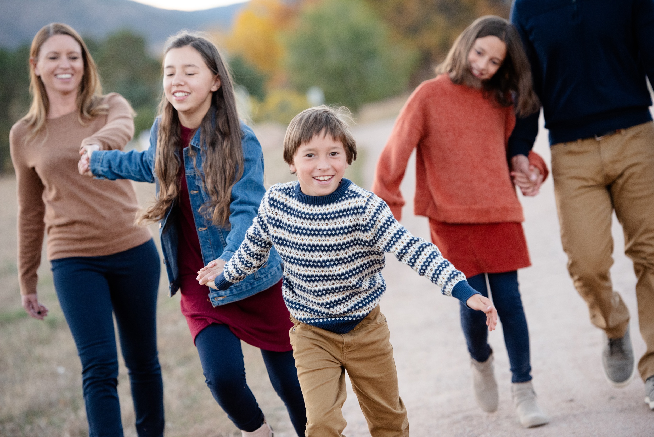 A young boy runs in front of a family holding hands in a park trail