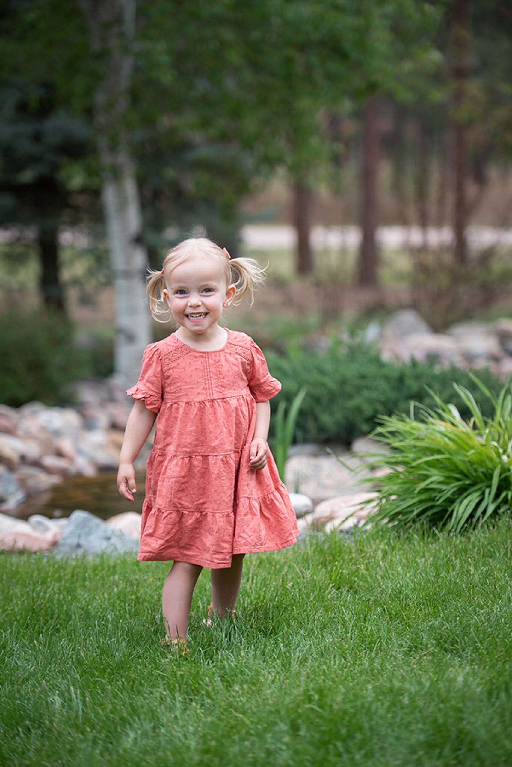 A toddler girl in a pink dress giggles while exploring a park lawn after visiting kids birthday party places denver