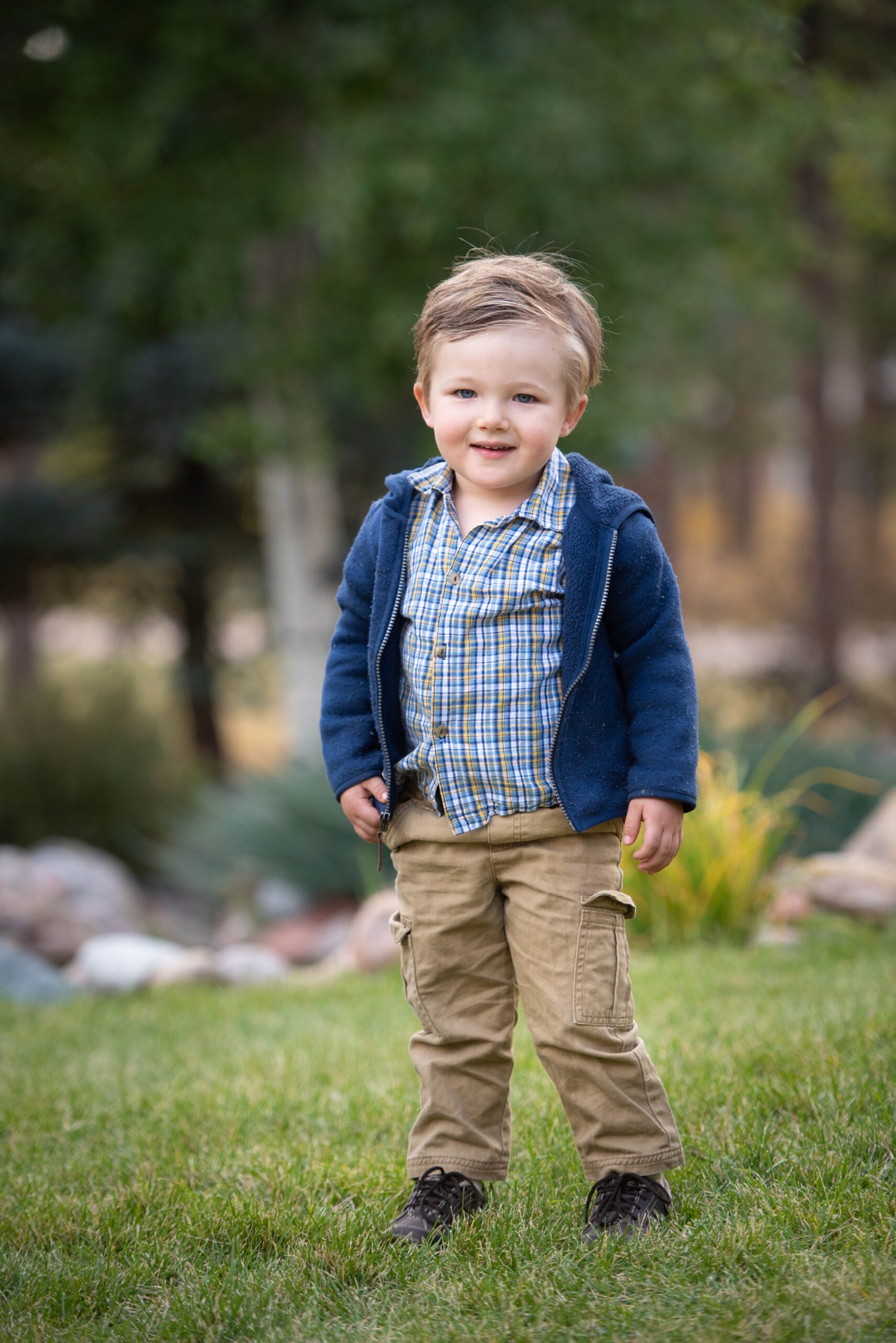 A toddler boy in khaki cargo pants and a blue hoodie smiles while exploring a park after visiting kids birthday party places denver