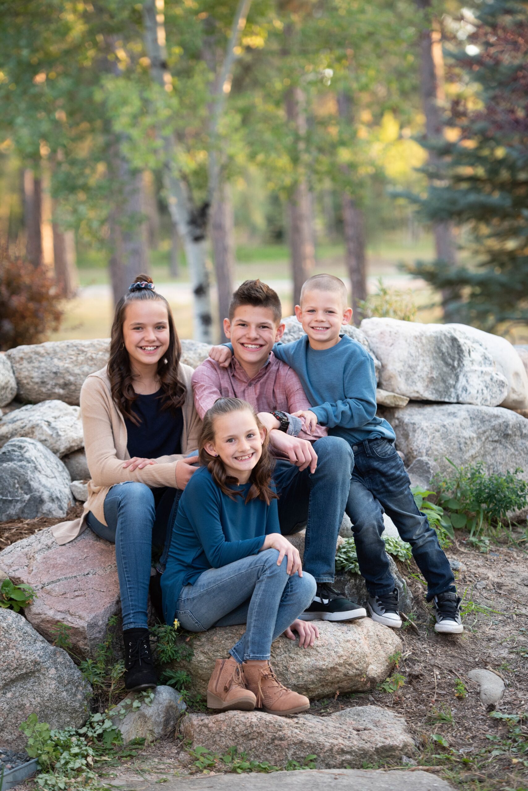 Four young happy siblings sit together on some boulders in one of the parks in Denver for kids