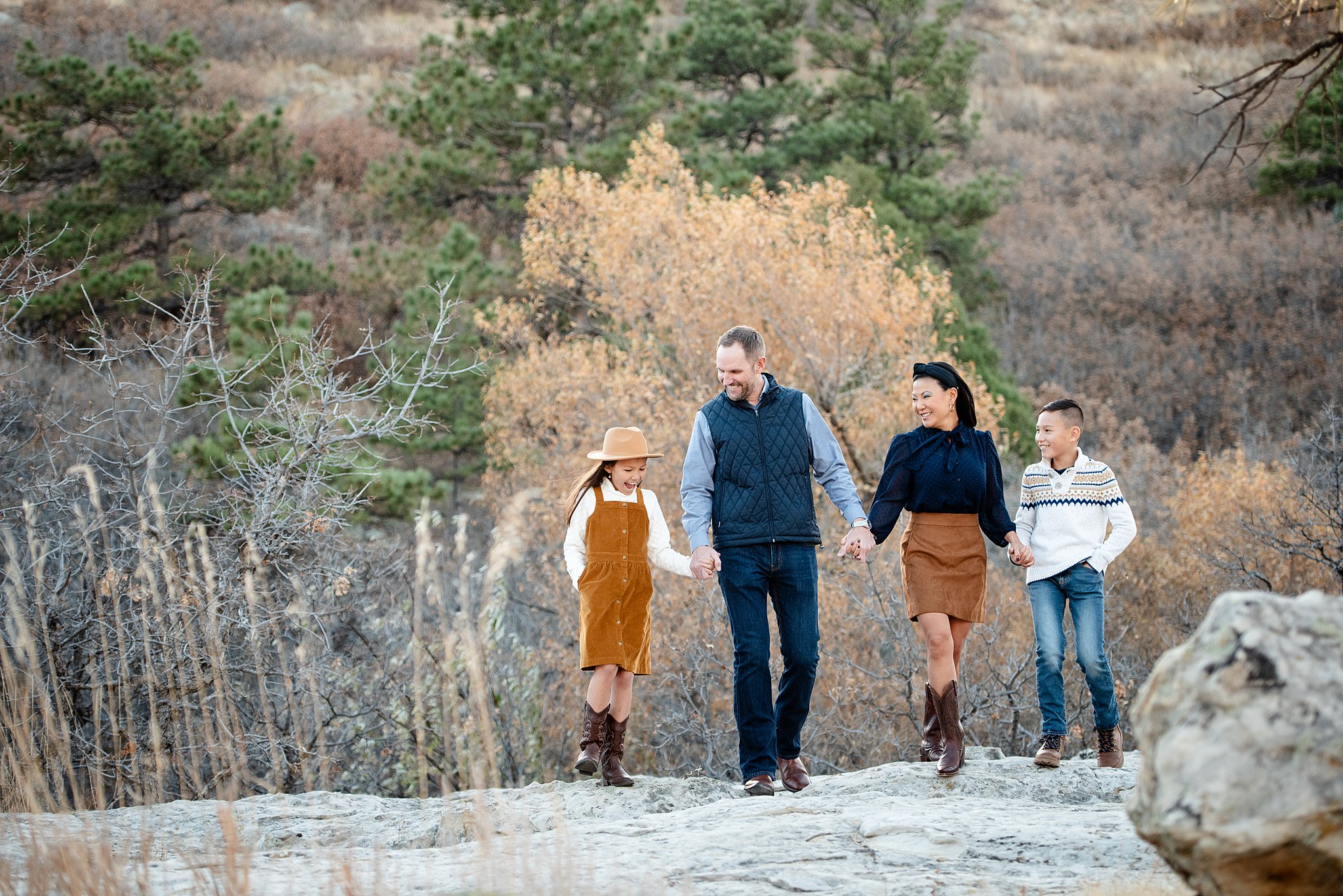 A mom and dad hold hadns with their young son and daughter as they explore a hike in the mountains