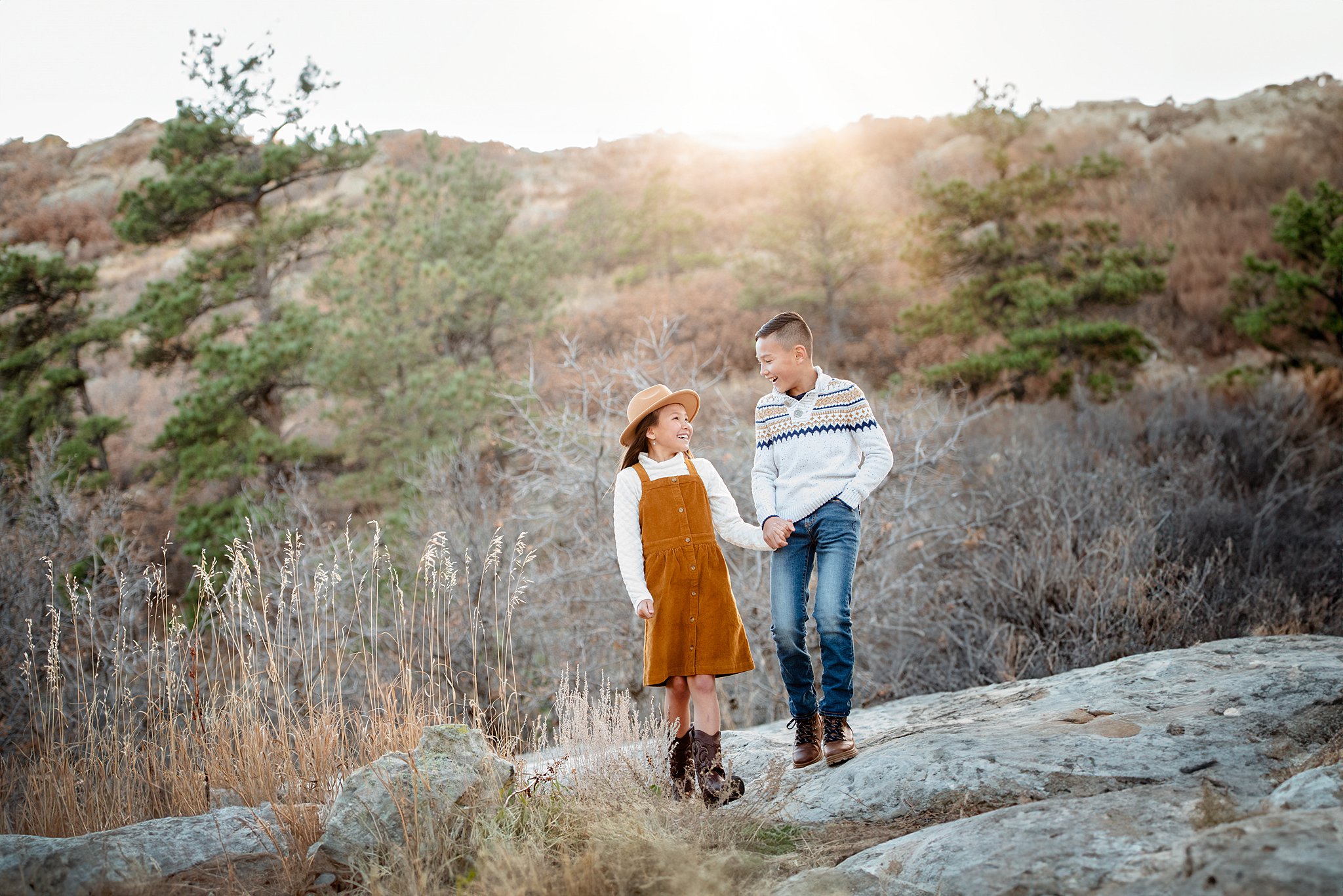 An older brother helps his younger sister on a hike by holding hands as they laugh at sunset after visiting a south denver pediatric dentist