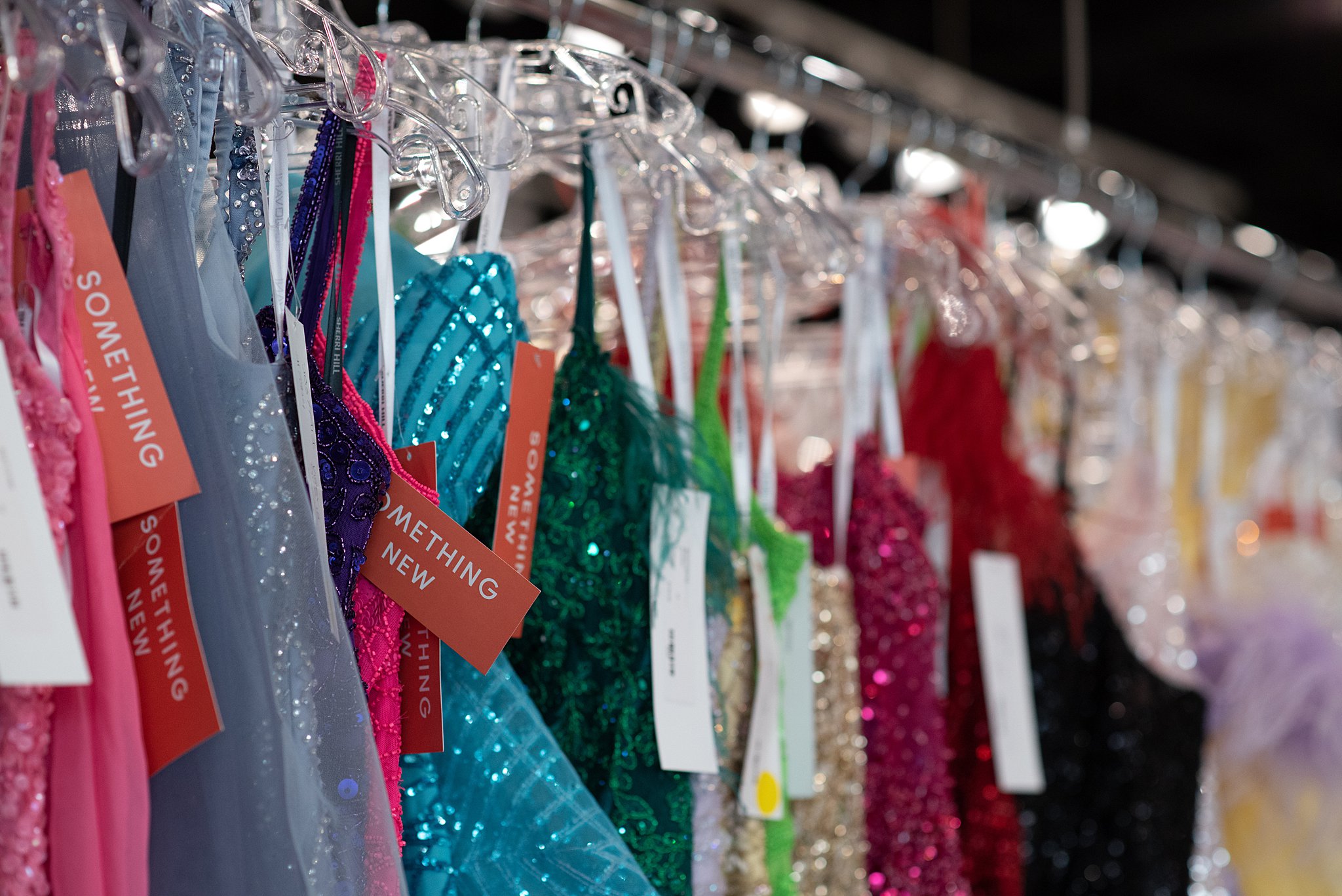 A row of prom dresses in colorado springs hang on a rack in a studio with tags