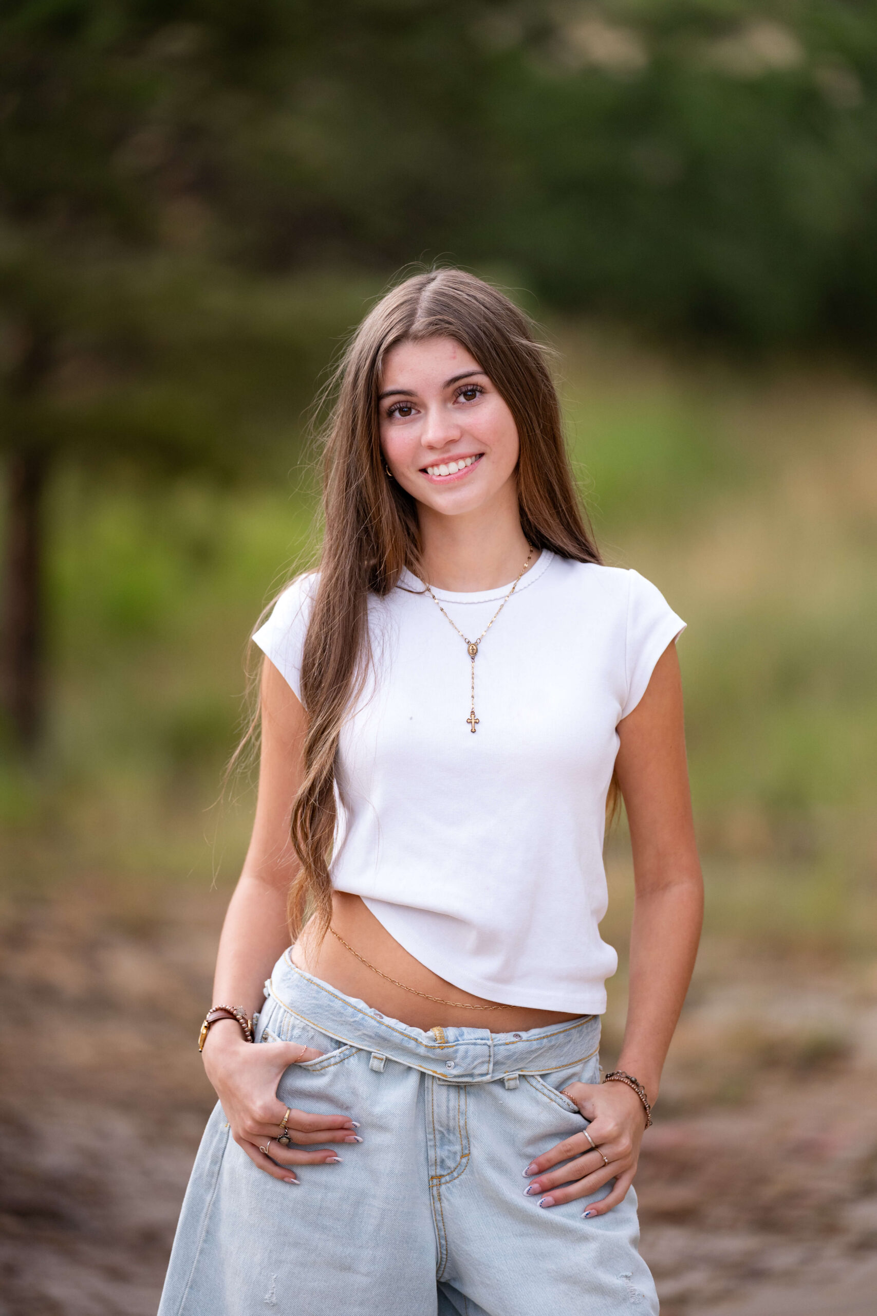 A smiling high school senior with thumbs in pants pockets and white blouse standing after visiting Colorado Springs Boutiques