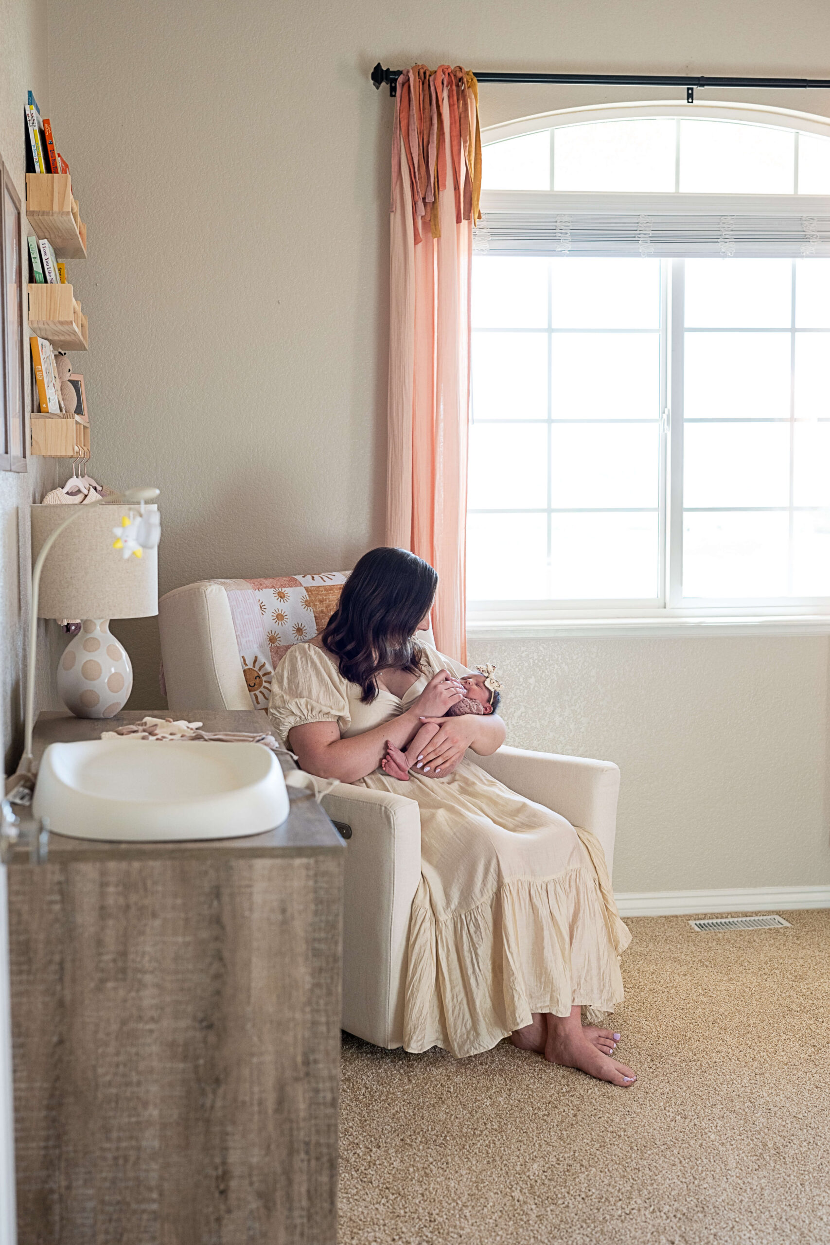 A new mom snuggles her newborn daughter in a nursing chair under a window in her nursery