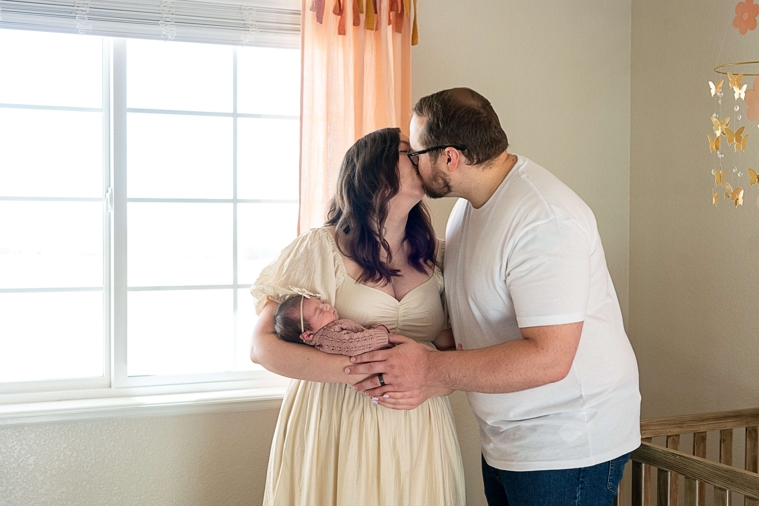 Happy new parents kiss while cradling their newborn in a nursery after meeting Flourish Collective