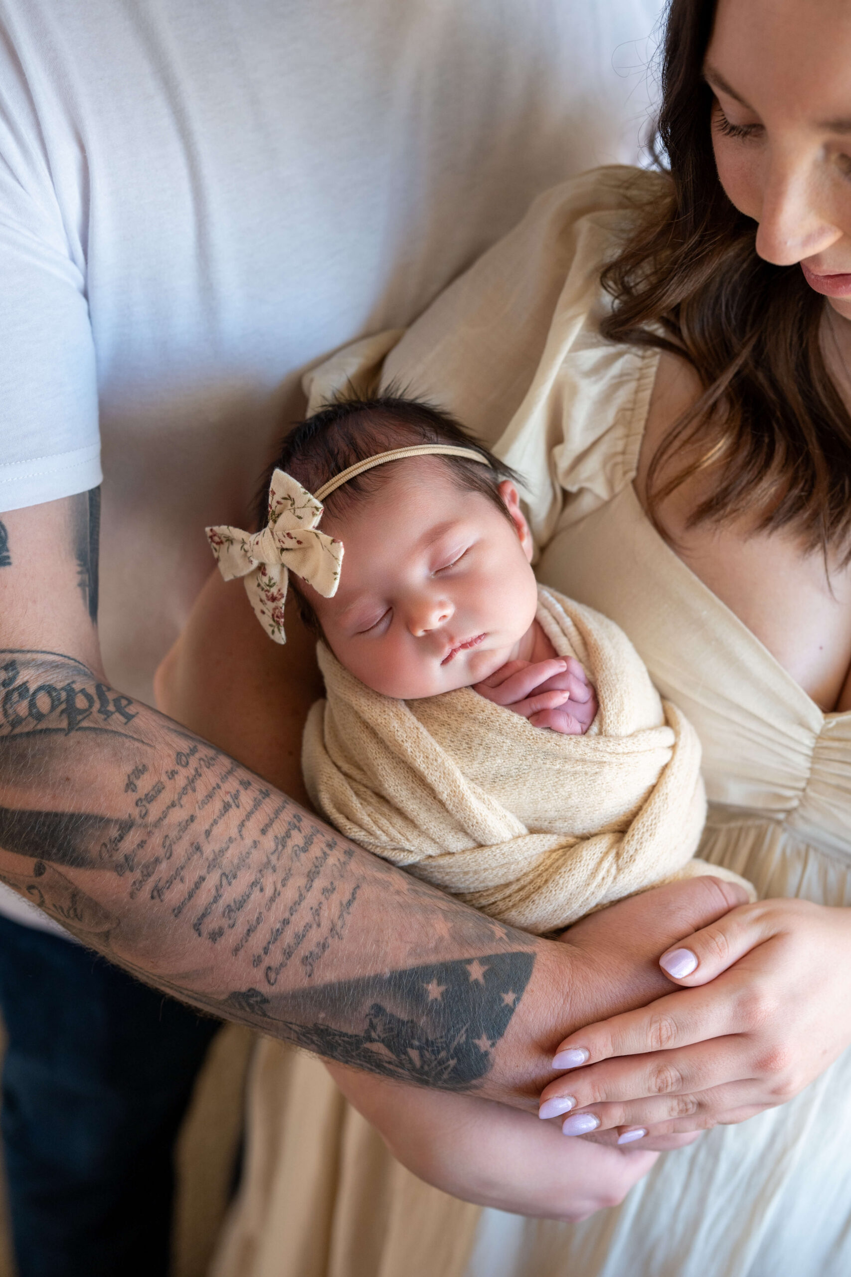 A newborn baby sleeps in mom's arms in a yellow swaddle and matching bow after meeting Flourish Collective