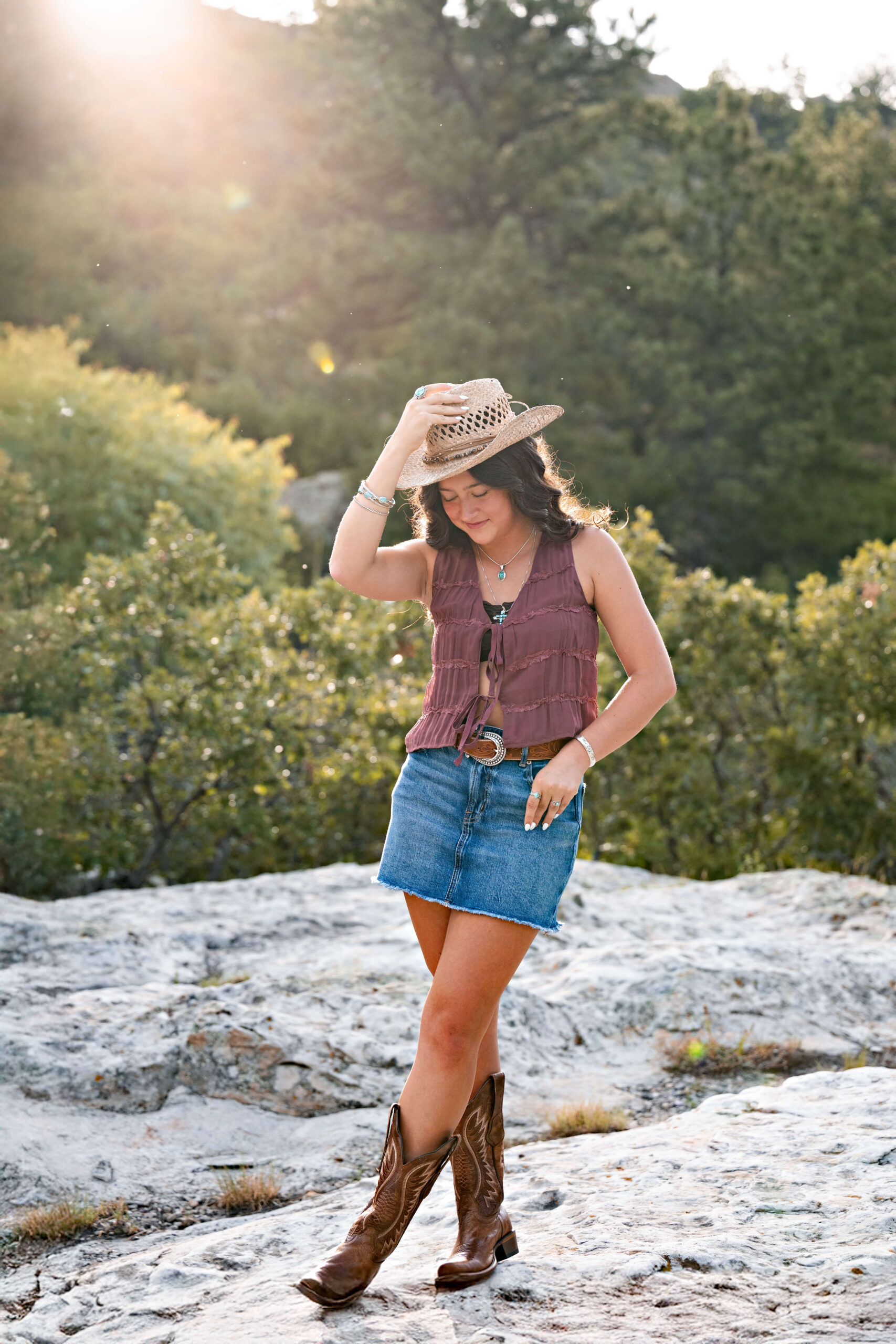 A high school senior places a cowboy hat on her head while looking down at the mountain boulder she is standing on before act prep in colorado springs.