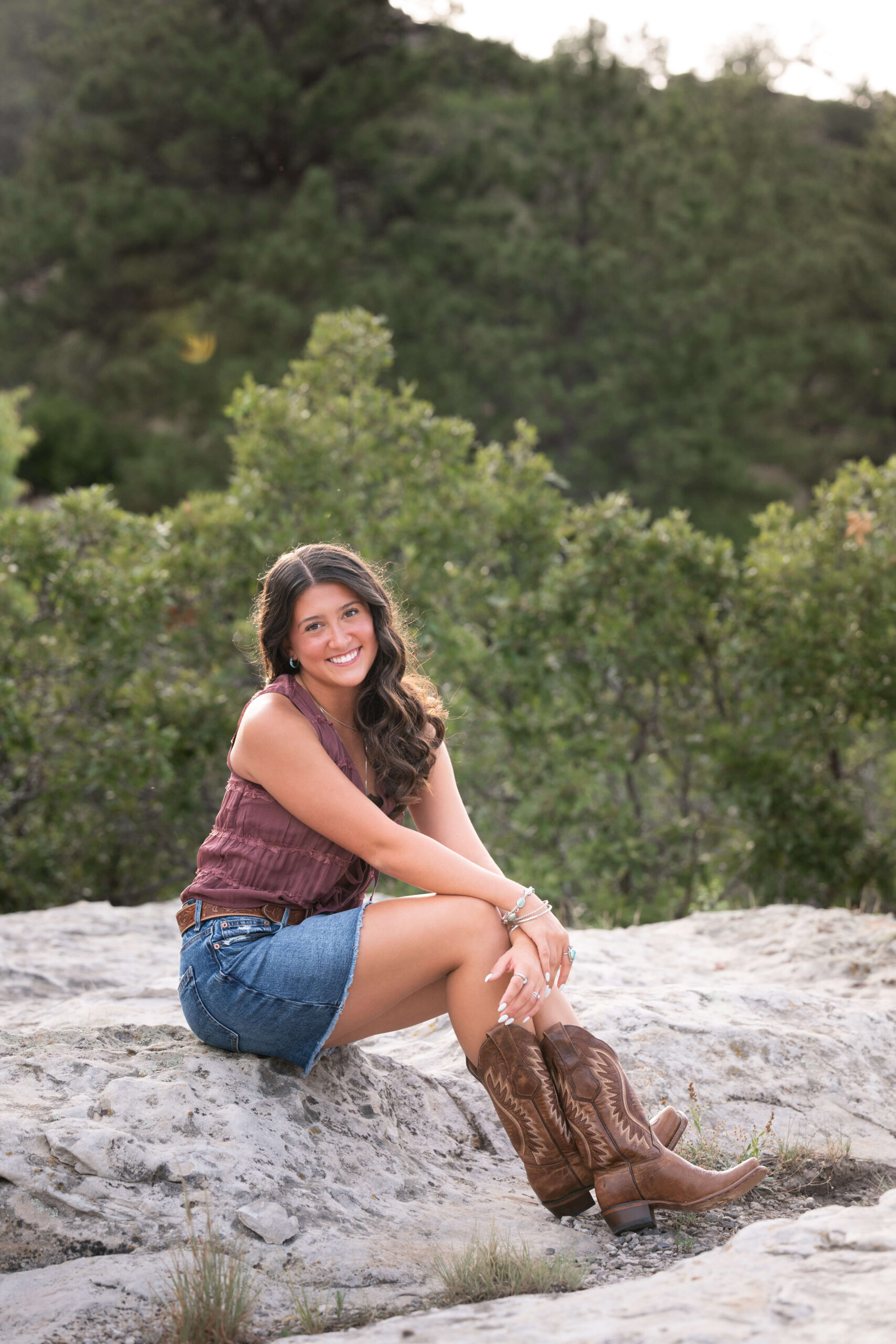 A high school senior in a jean skirt and cowgirl boots sits on. a rock in the mountains after finding act prep in colorado springs.
