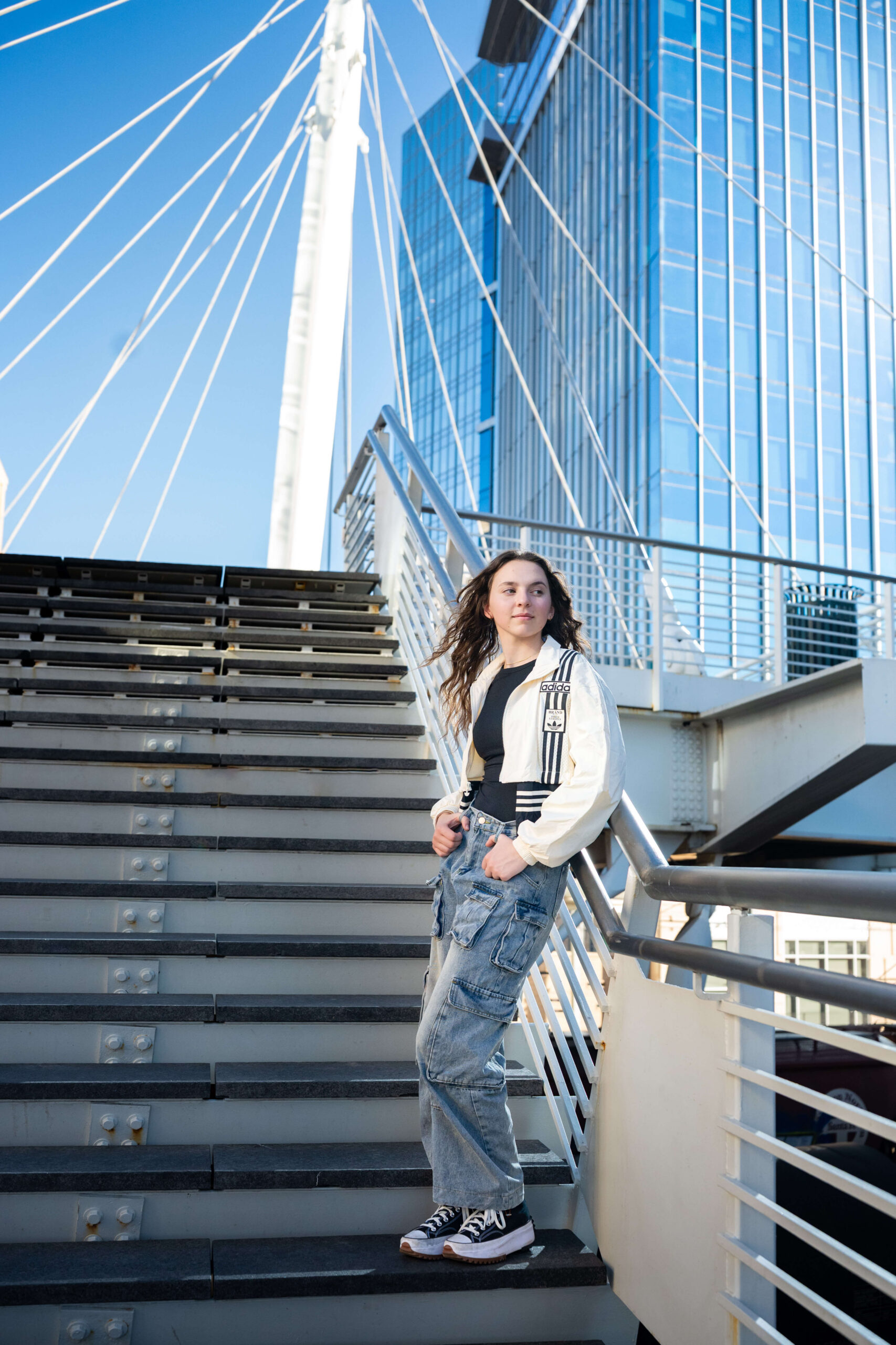 A high school senior leans against a railing of a staircase, staring off into the distance of a city.