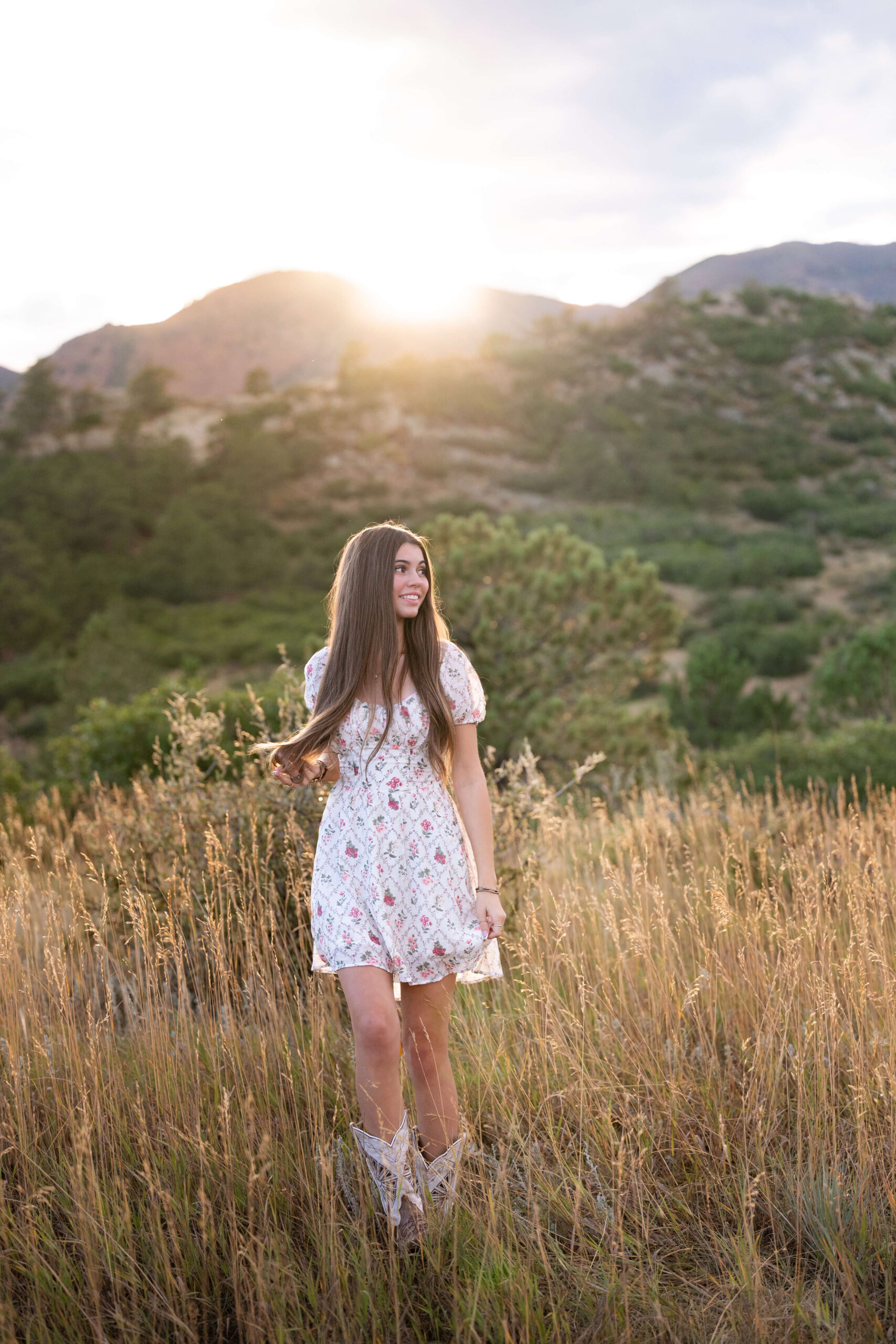 A smiling high school senior in a floral dress stares into the distance of the mountains for colorado springs senior photos.