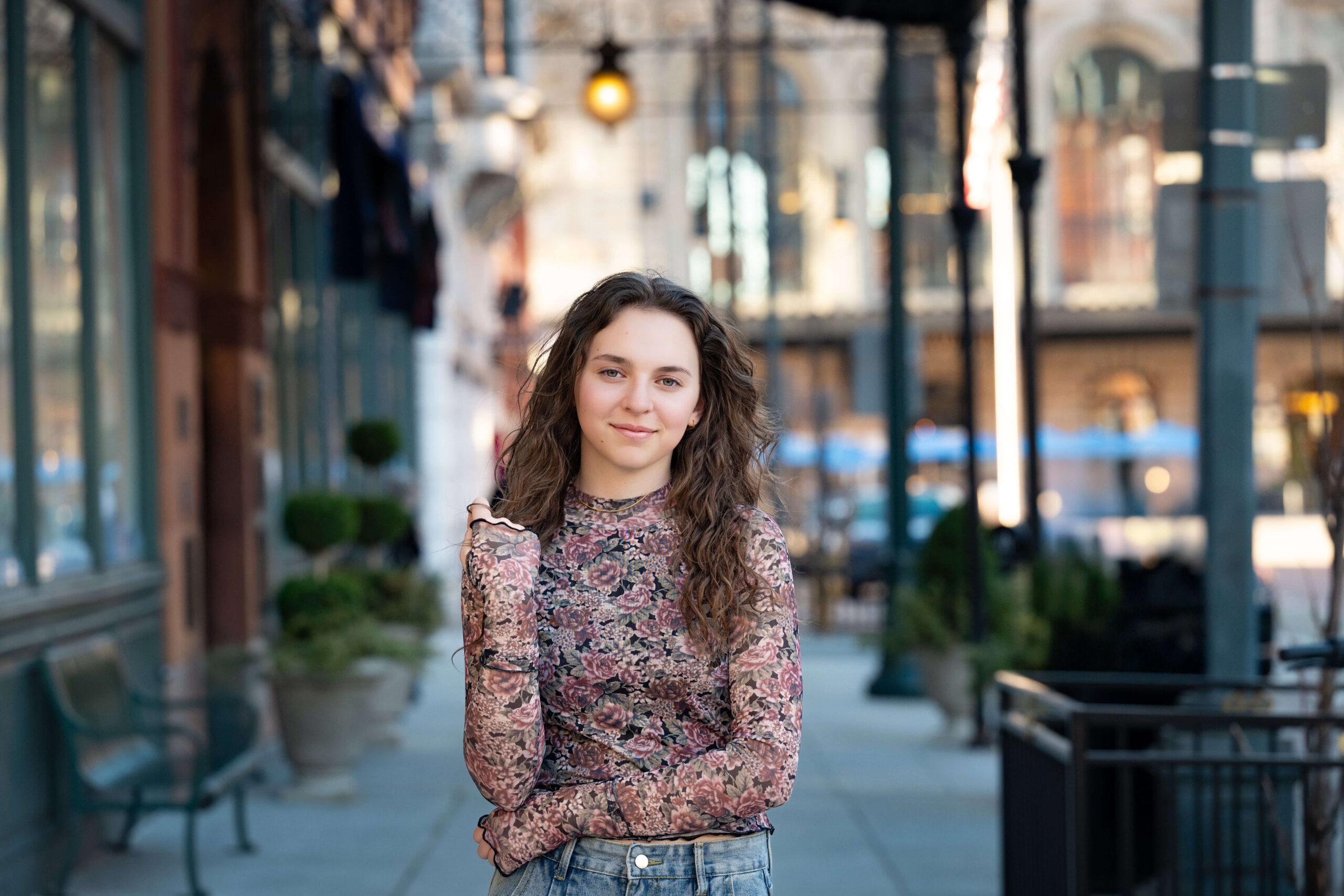A high school senior stands on a city road while playing with her hair during colorado springs senior photos in a flower print blouse.