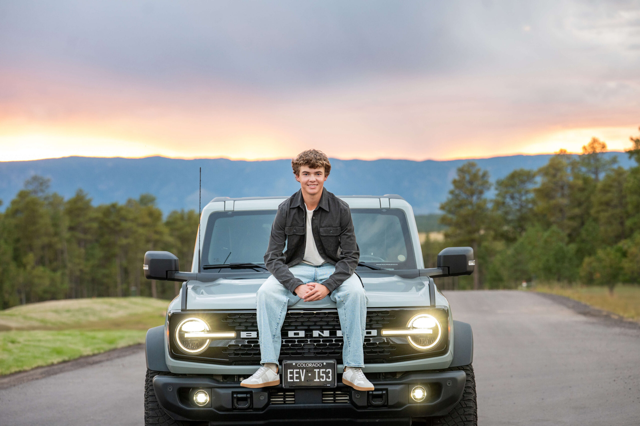 A high school senior sits on his Ford Bronco at sunset after exploring graduation party venues in colorado springs.