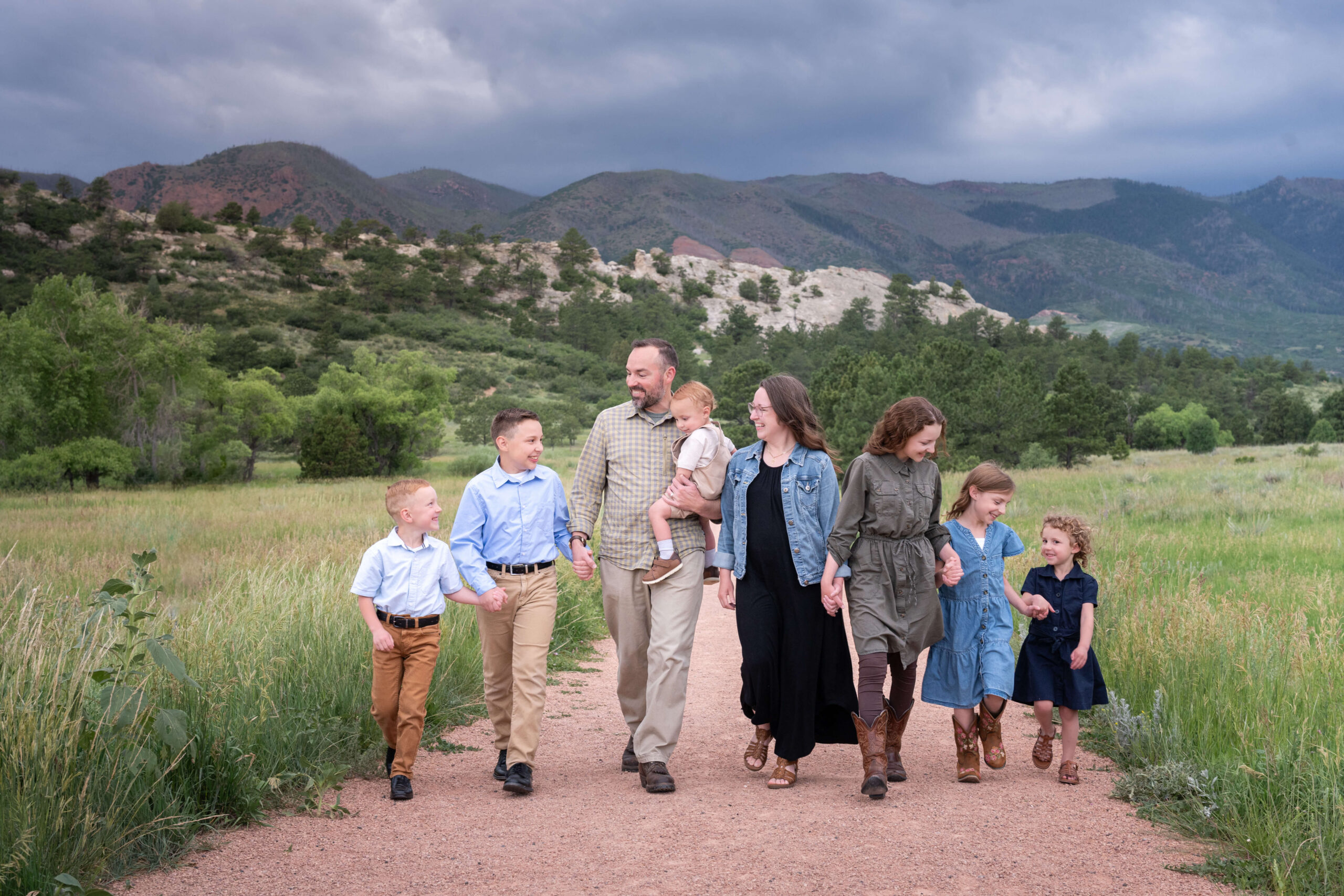 A mom and dad walk in a mountain trail holding hands and laughing with their six children after finding indoor playgrounds in colorado springs