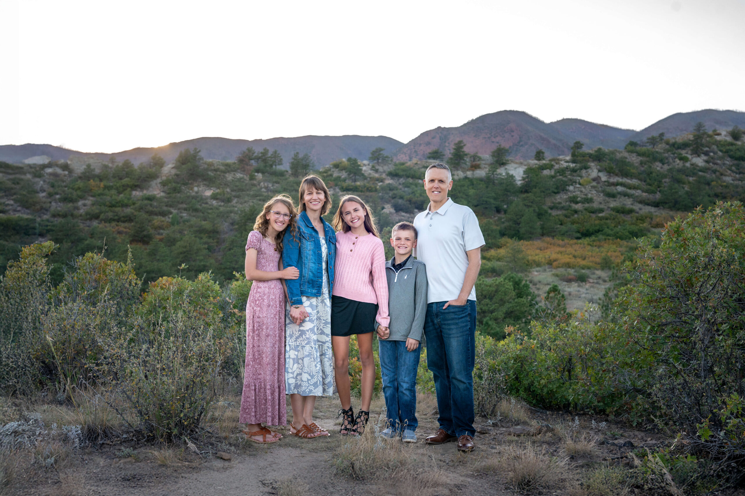 A mom and dad stand smiling with their three pre teen children in the mountains at sunset after finding pediatricians in colorado springs