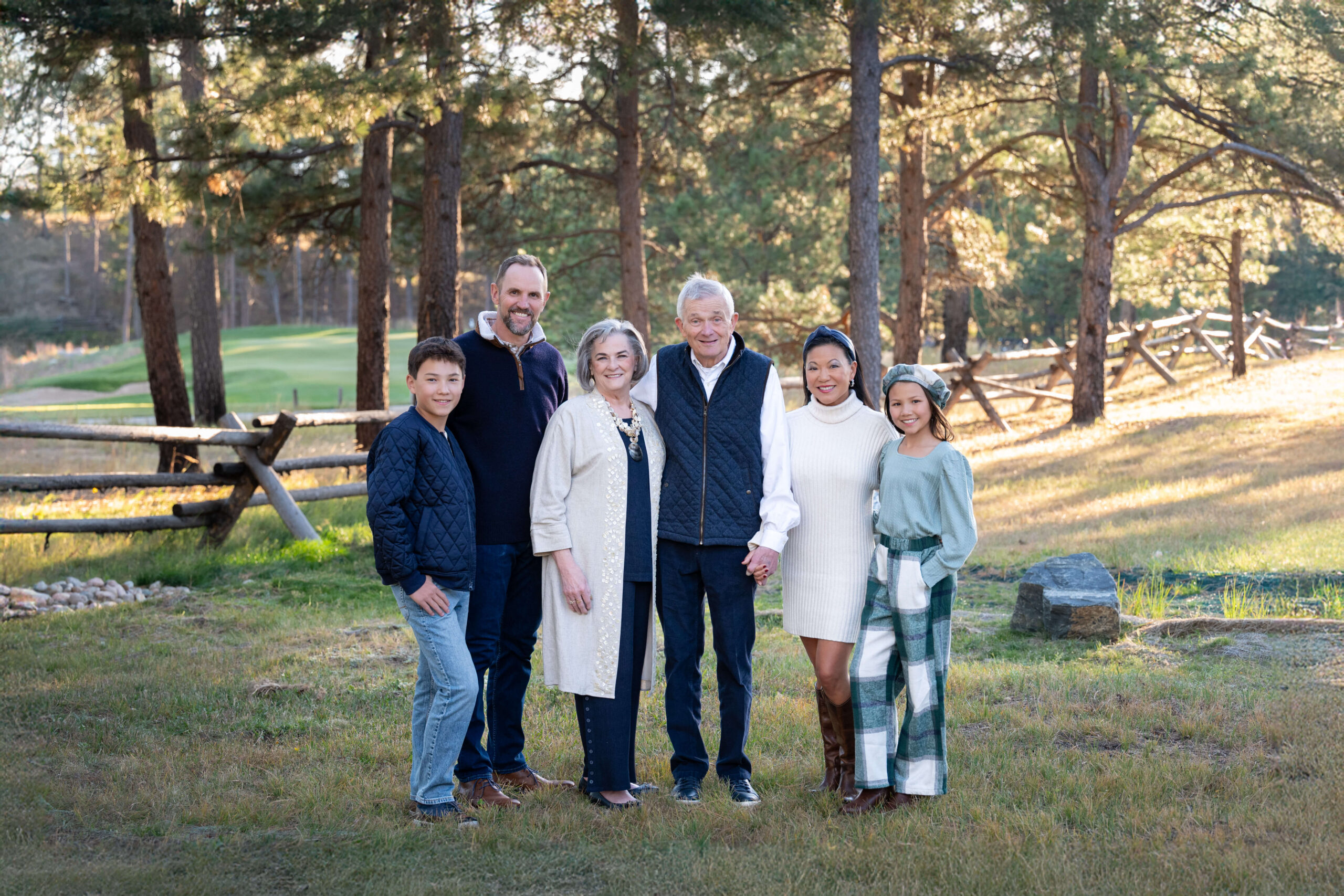 Three generations of family stand in a park smiling and holding hands at sunset after finding playgrounds in colorado springs