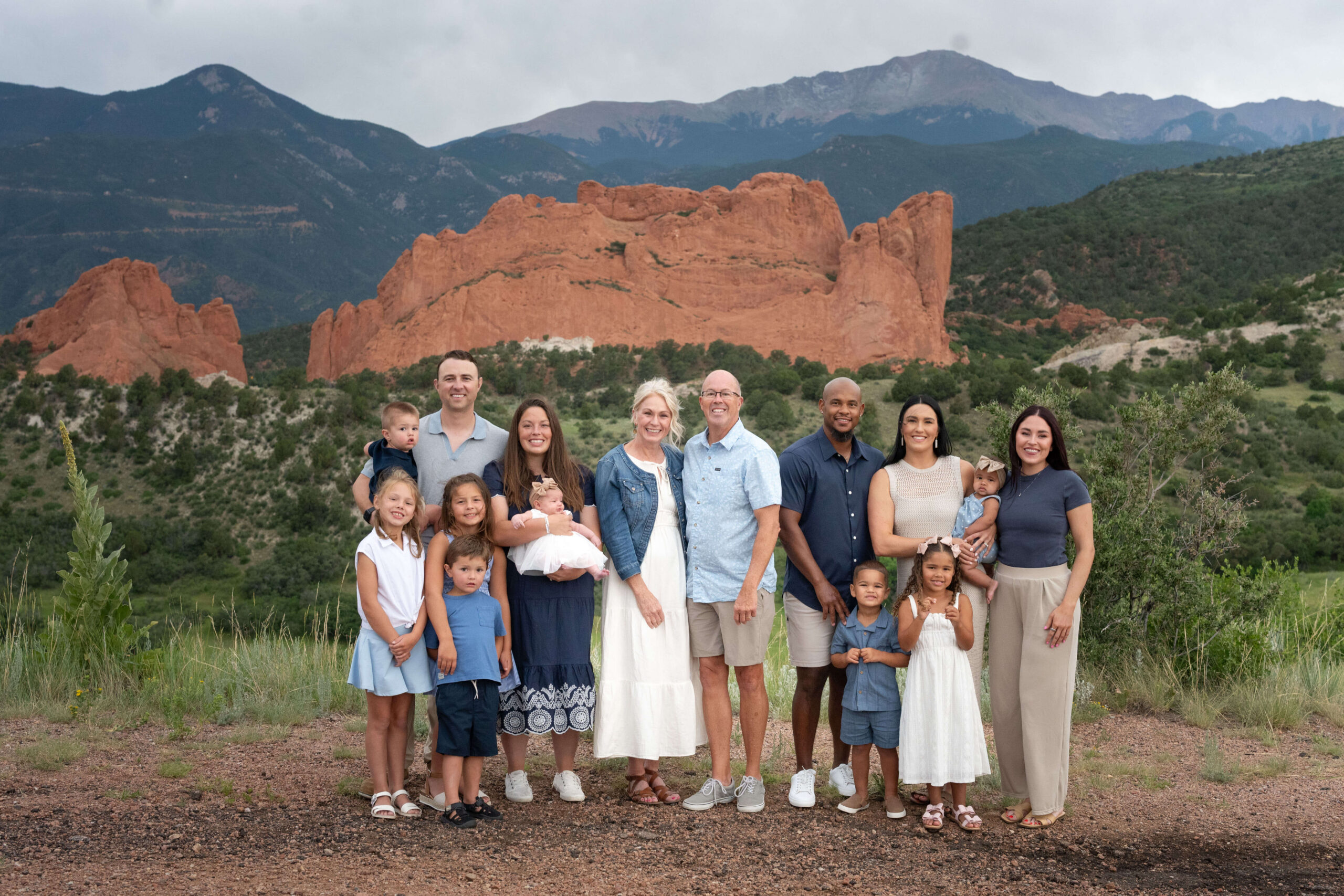 A happy extended family stands on a mountain overlook smiling with babies and young children after exploring preschools in colorado springs