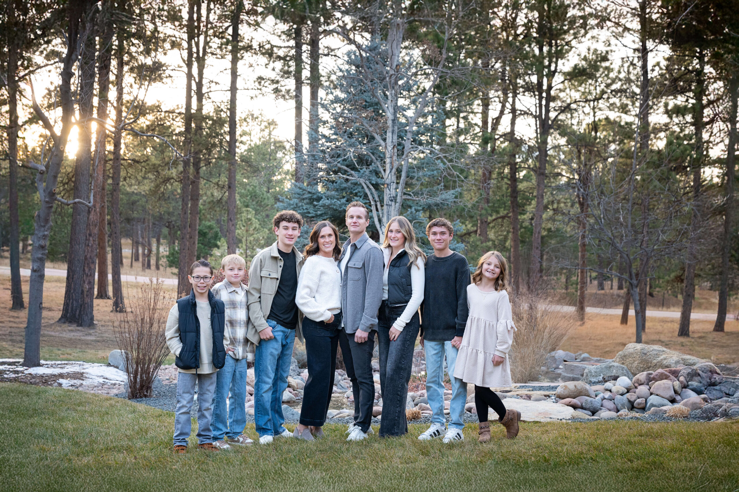 A mom and dad stand surrounded by their six children at sunset in a park with big smiles after enjoying preschools in colorado springs